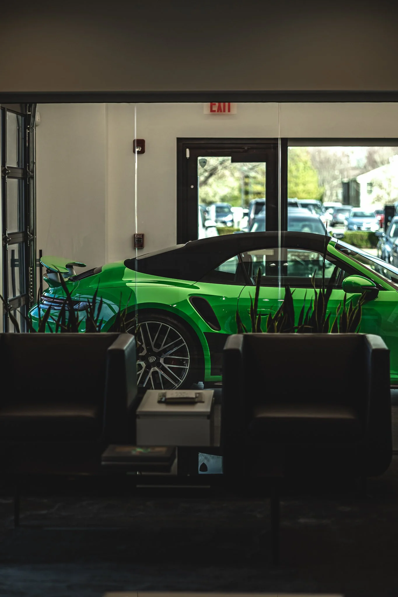 Inside a building, looking through a glass window at a bright green sports car parked outside