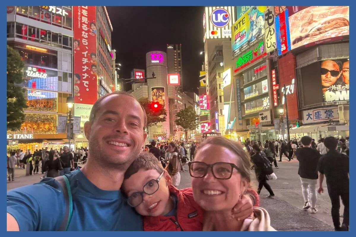Family selfie at Shibuya Crossing in Tokyo at night, surrounded by neon signs and crowds