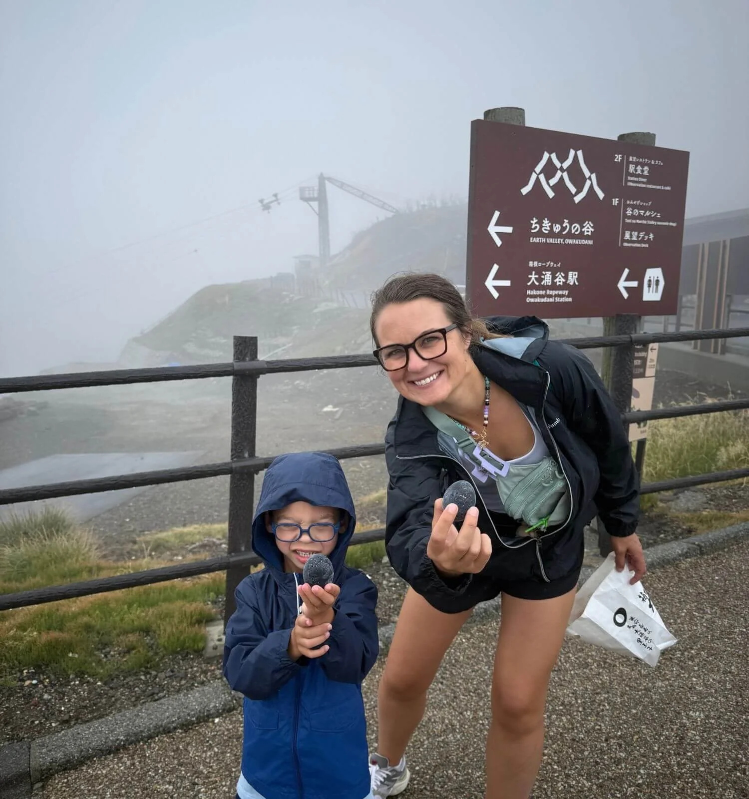 Mother and son holding black eggs in the fog at Owakudani volcanic valley, Japan
