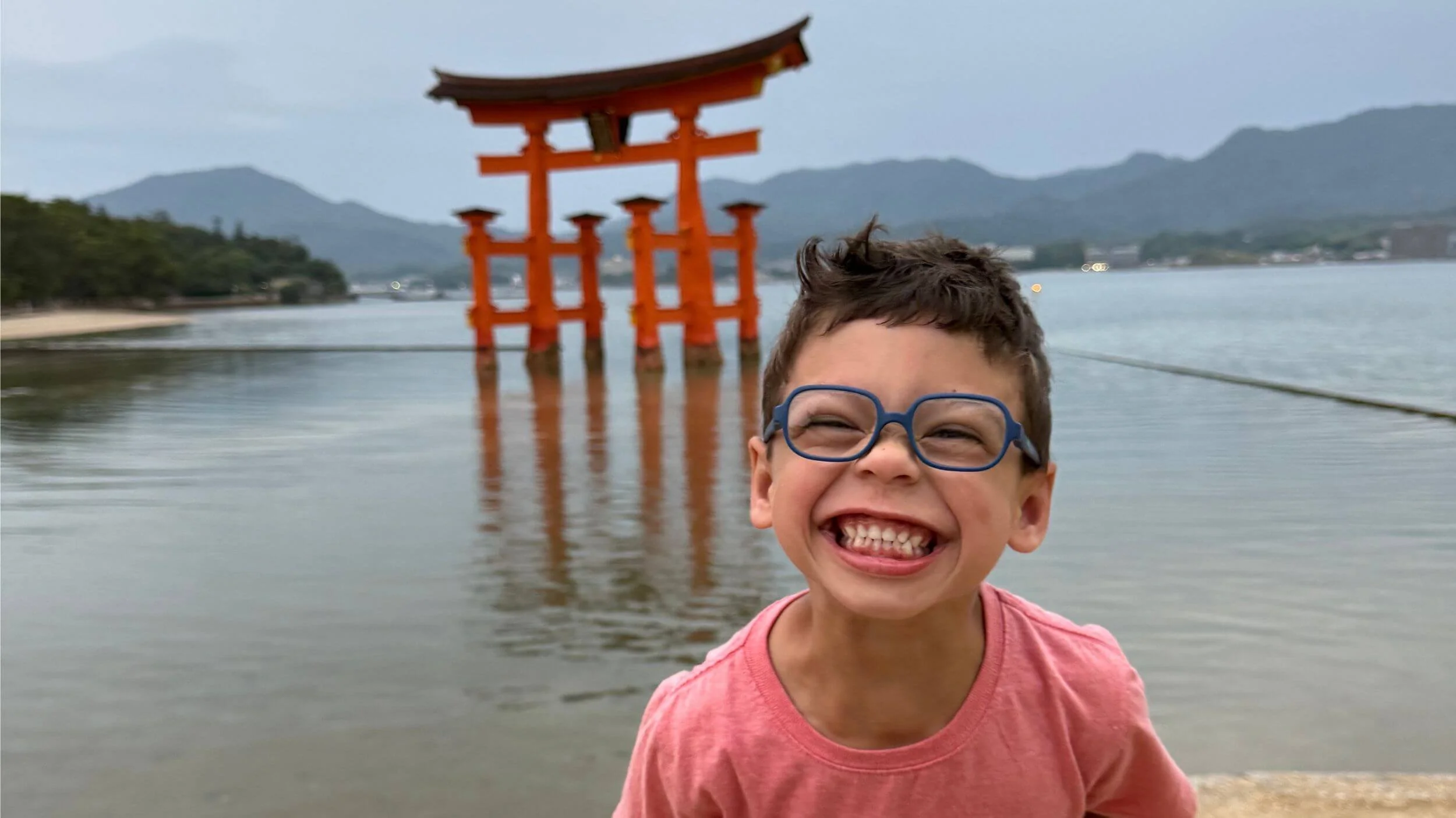 Young boy laughing hysterically in front of the floating torii gate on Miyajima, Japan