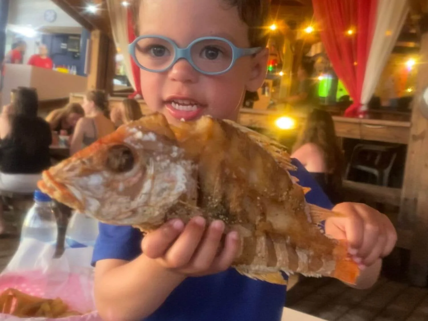 Toddler holding a whole fried fish at Zeerovers in Aruba.