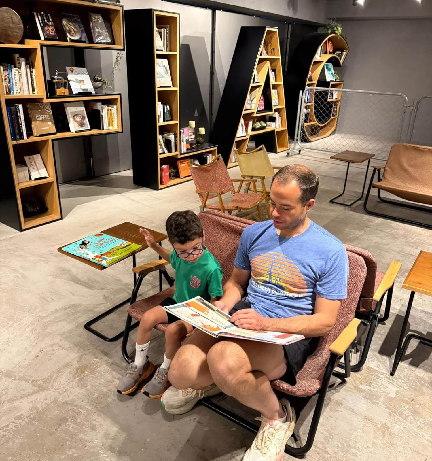 A father and son sitting together reading a book in the library at their hotel in Osaka, Japan.