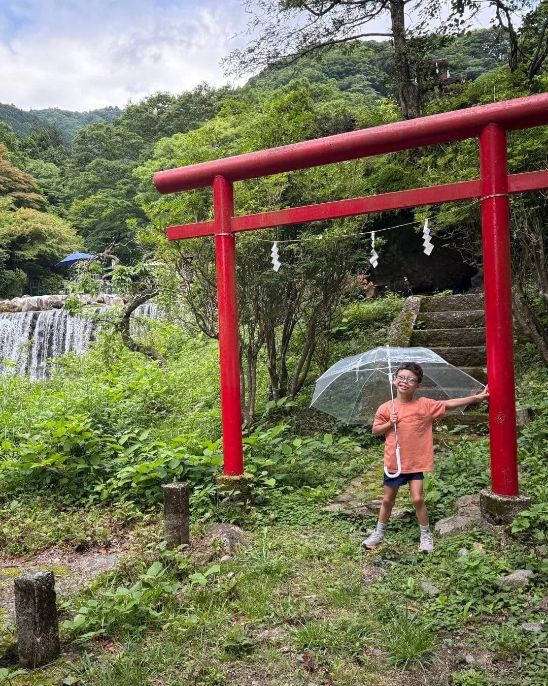 Child standing under a torii gate near a waterfall in Japan - watch our travel channel