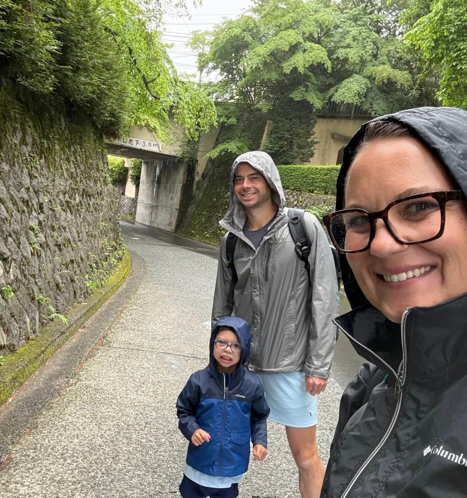 Family of three wearing rain jackets while walking through Hakone, Japan in the rain
