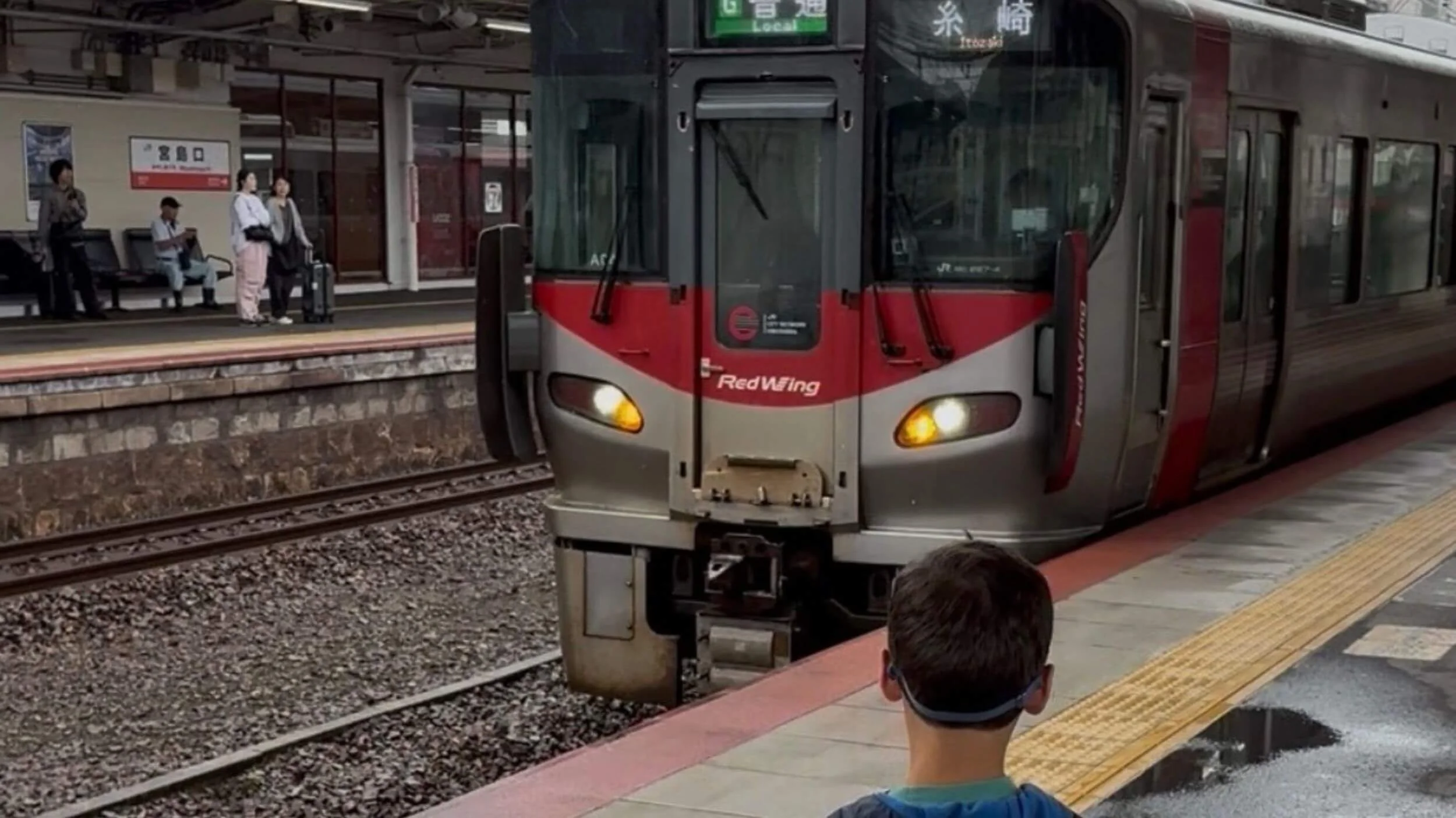 Young boy watching a local train arrive at Miyajimaguchi Station platform in Japan