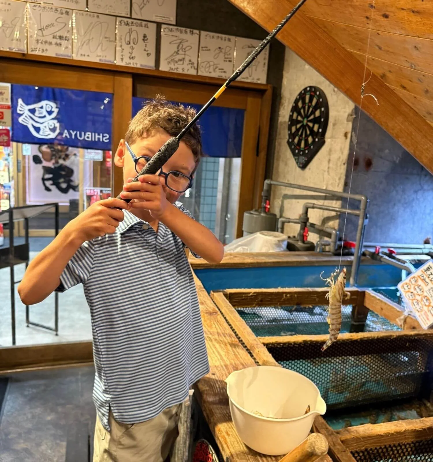 A young boy excitedly holding a freshly caught prawn at Zauo, a fishing restaurant in Tokyo, Japan, where guests catch their own seafood before it's cooked.