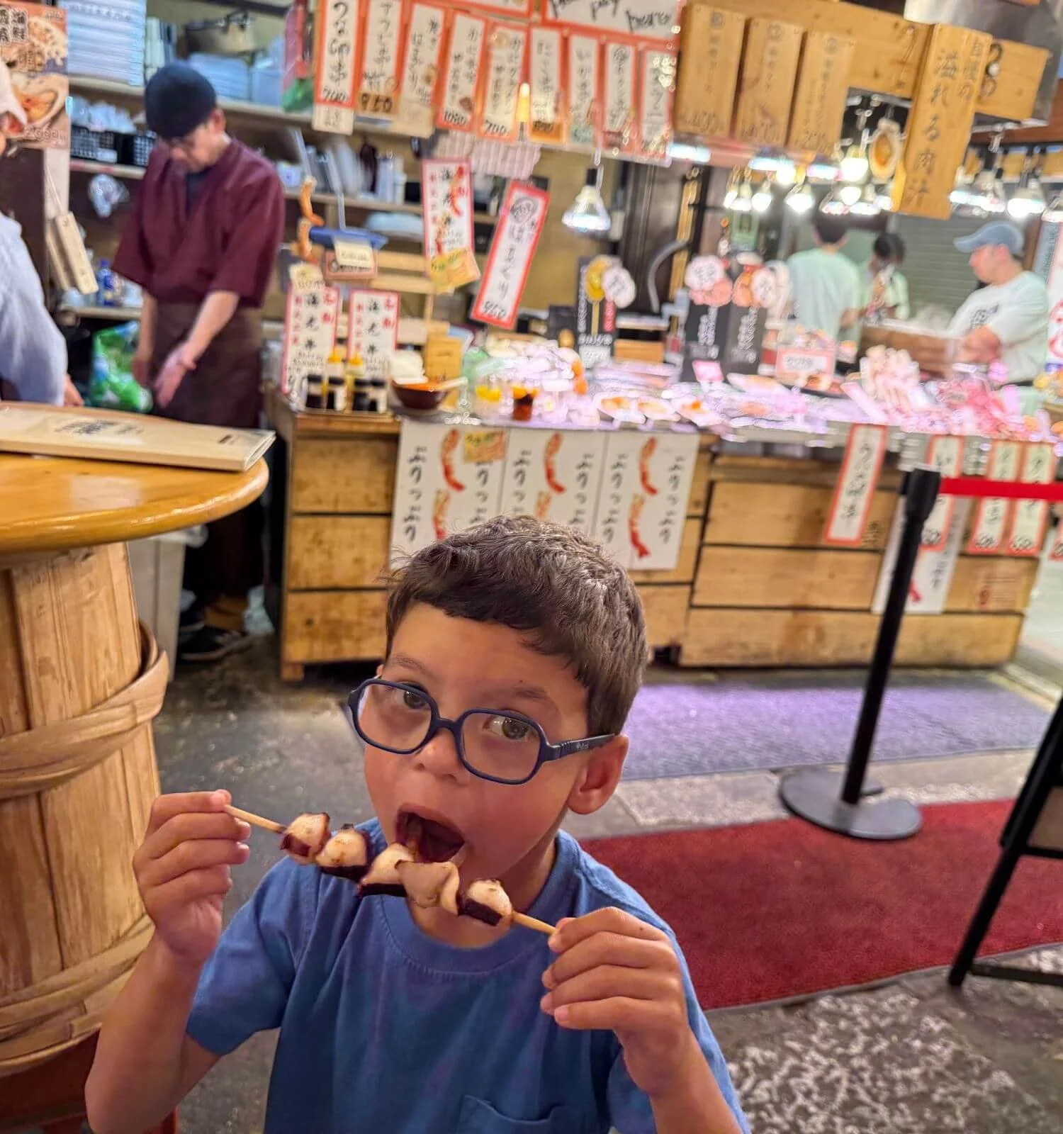 Young boy eating a grilled skewer at Nishiki Market in Kyoto, Japan