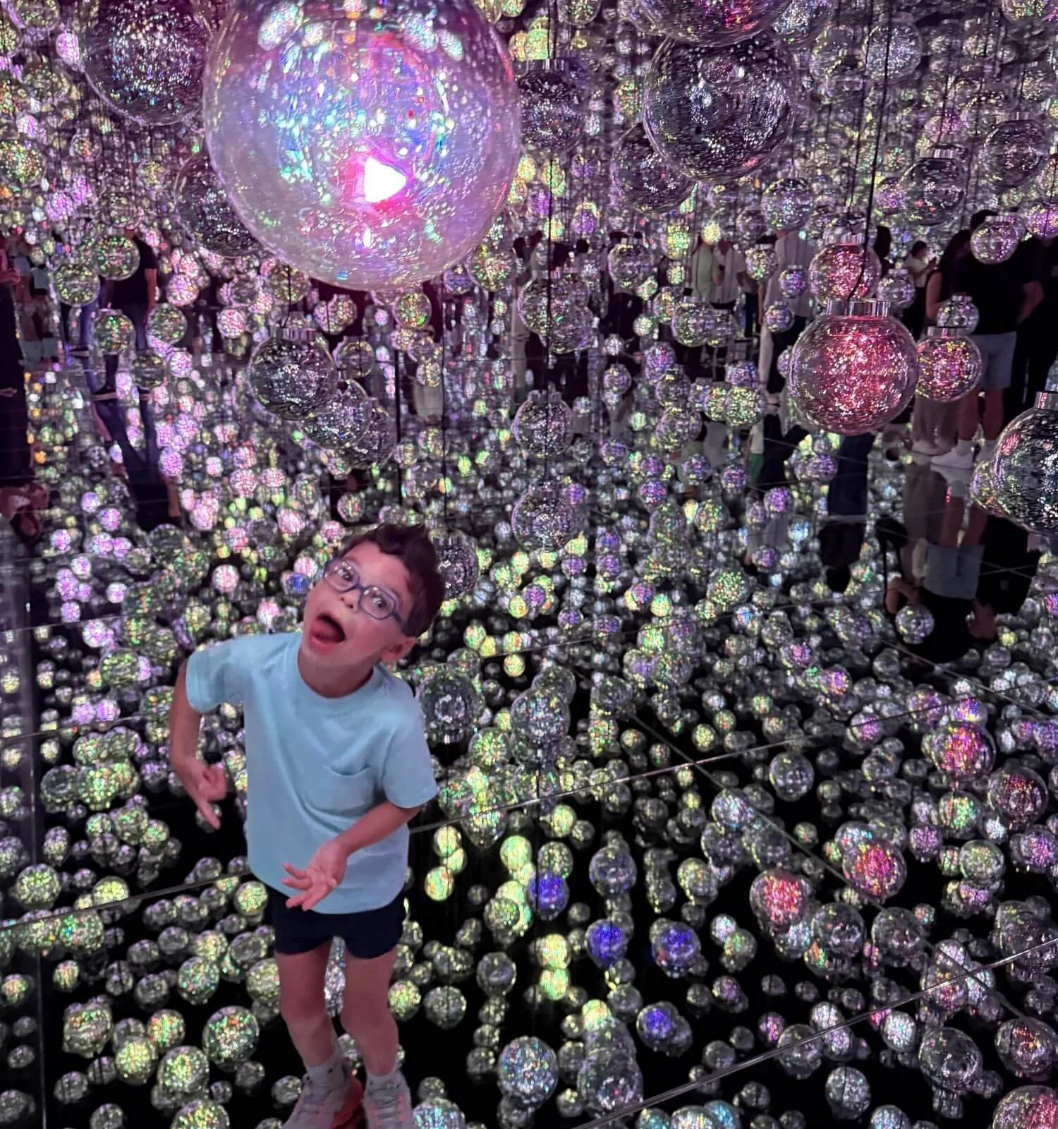 A young boy being silly among hundreds of glowing orbs in the mirrored globe room at teamLab Borderless in Tokyo, Japan.