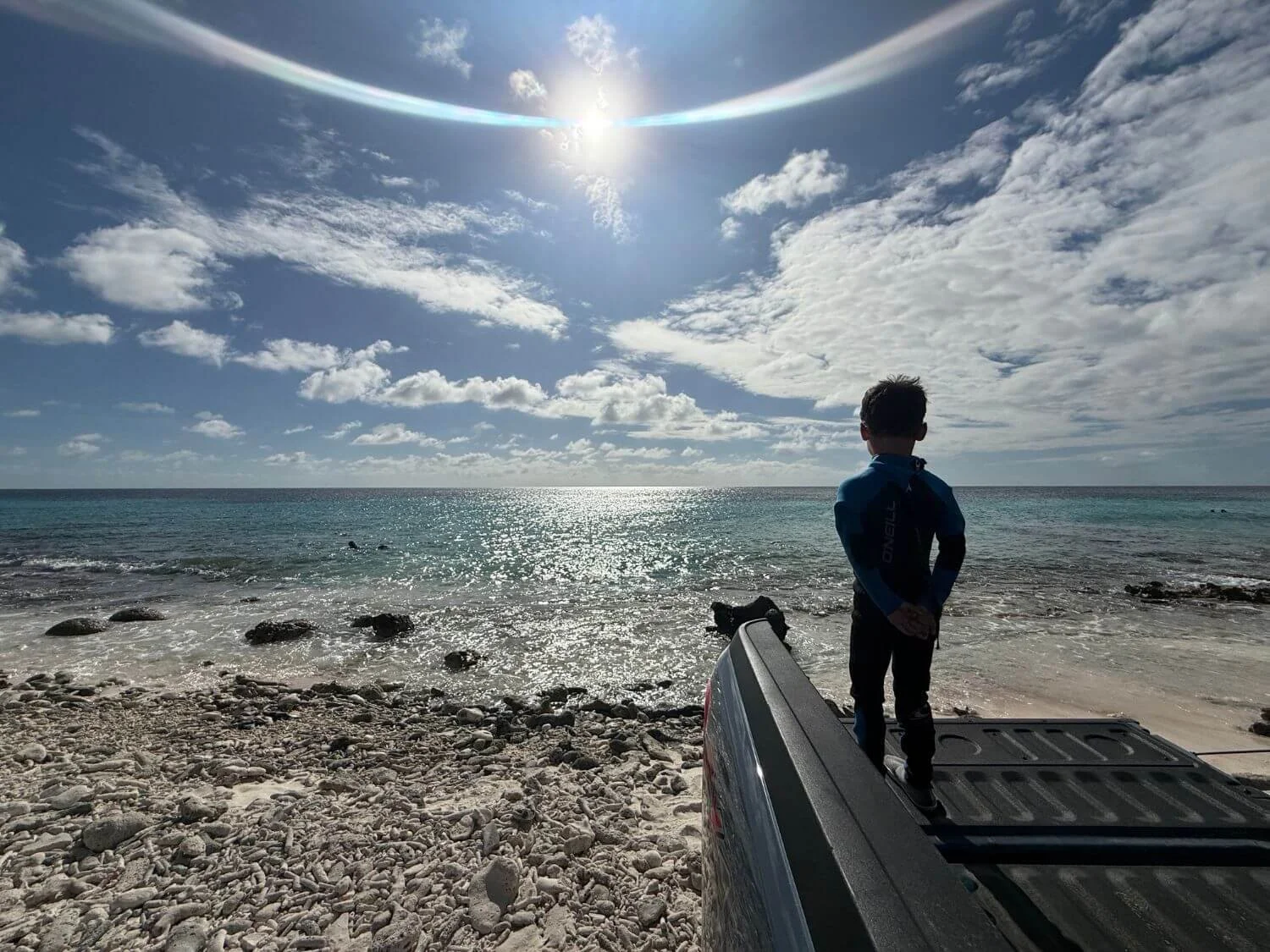 Boy in snorkel gear in the back of a truck parked next to the shore in Bonaire.