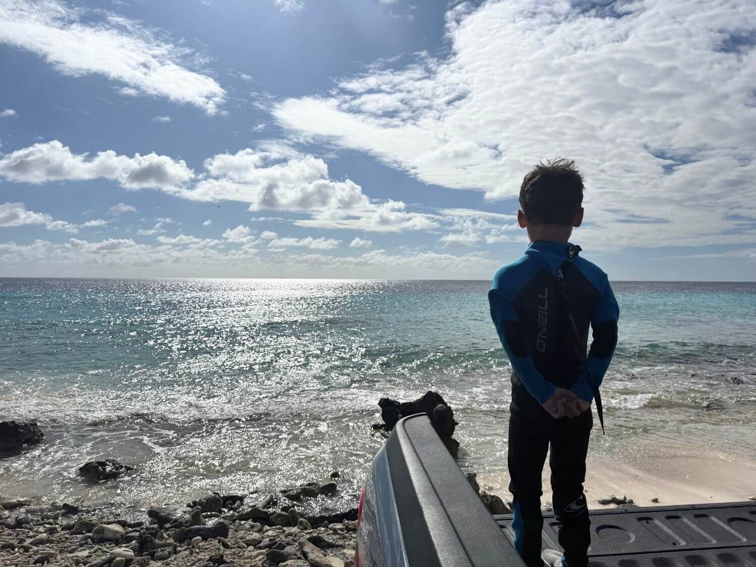 Boy in a wetsuit standing on a truck tailgate at Pink Beach in Bonaire.