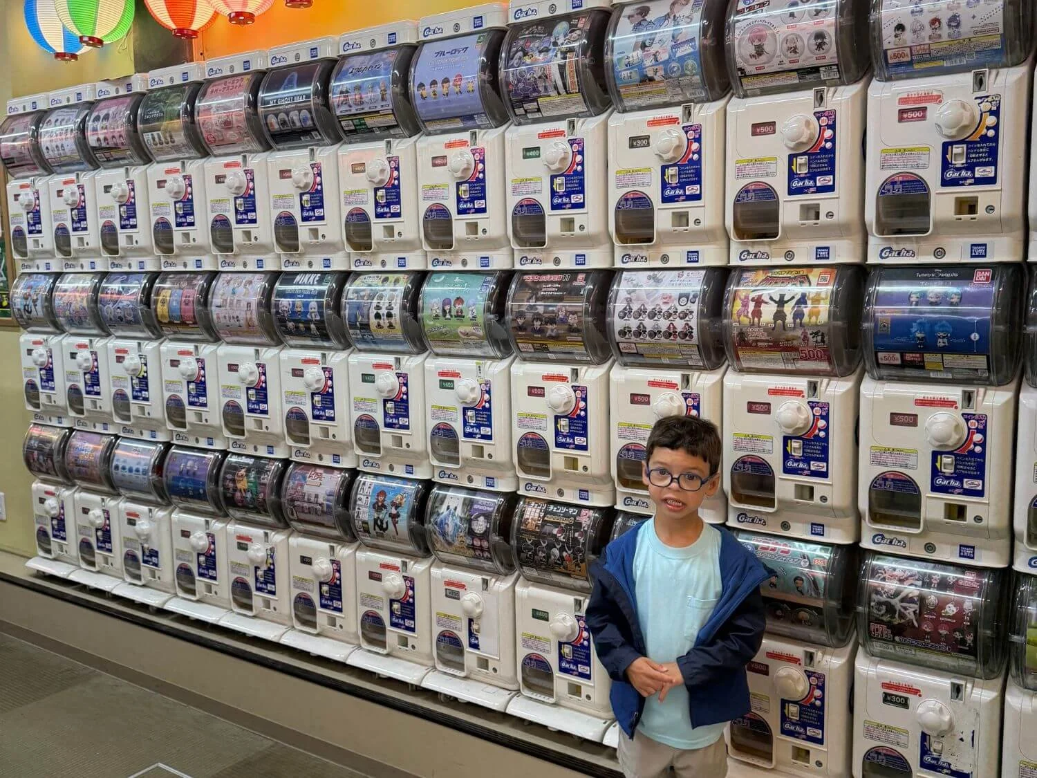 Boy in front of a wall of capsule toy machines in Osaka Japan.