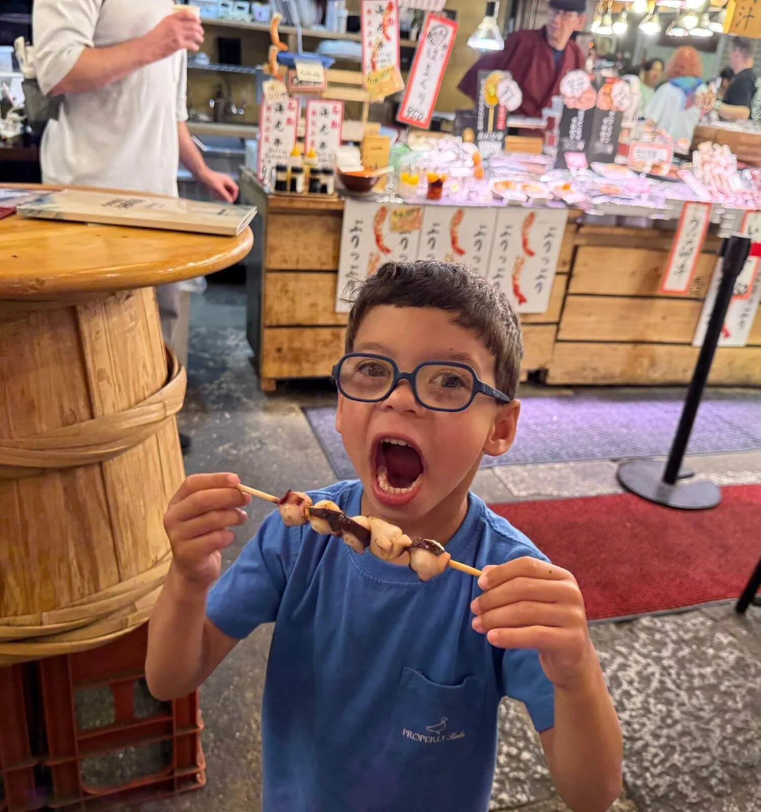 A young boy eating a seafood skewer at Nishiki Market in Kyoto, Japan.