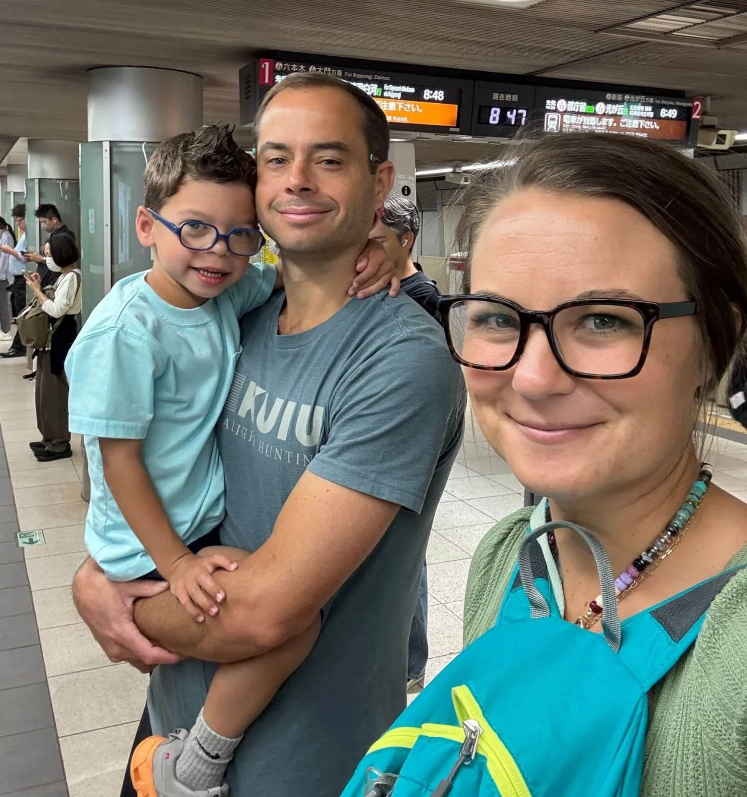 Family of three at a Tokyo train station platform, backpack worn on the front for train etiquette