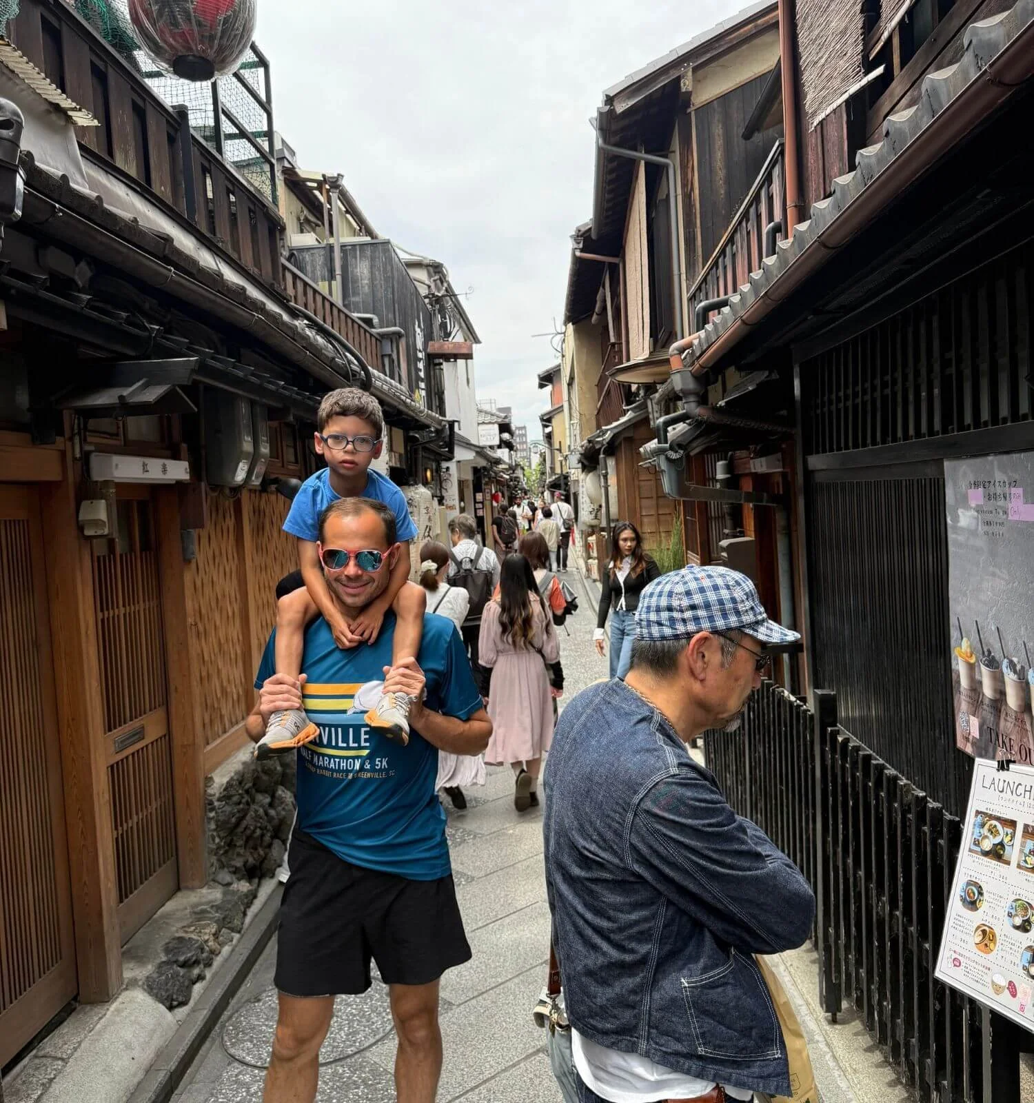 A young boy sitting on his dad's shoulders while exploring a downtown street in Kyoto, Japan.
