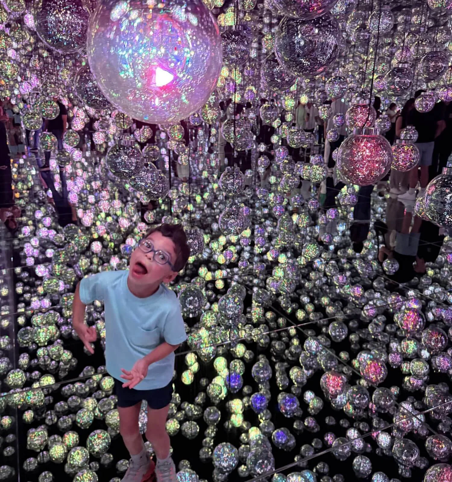 Young boy reacting with excitement inside a mirrored room filled with illuminated glass orbs at TeamLab Borderless in Tokyo, Japan