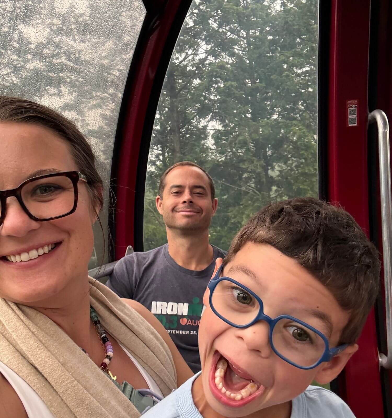 A family of three taking a selfie on the Hakone ropeway gondola, with the young boy making a funny face.