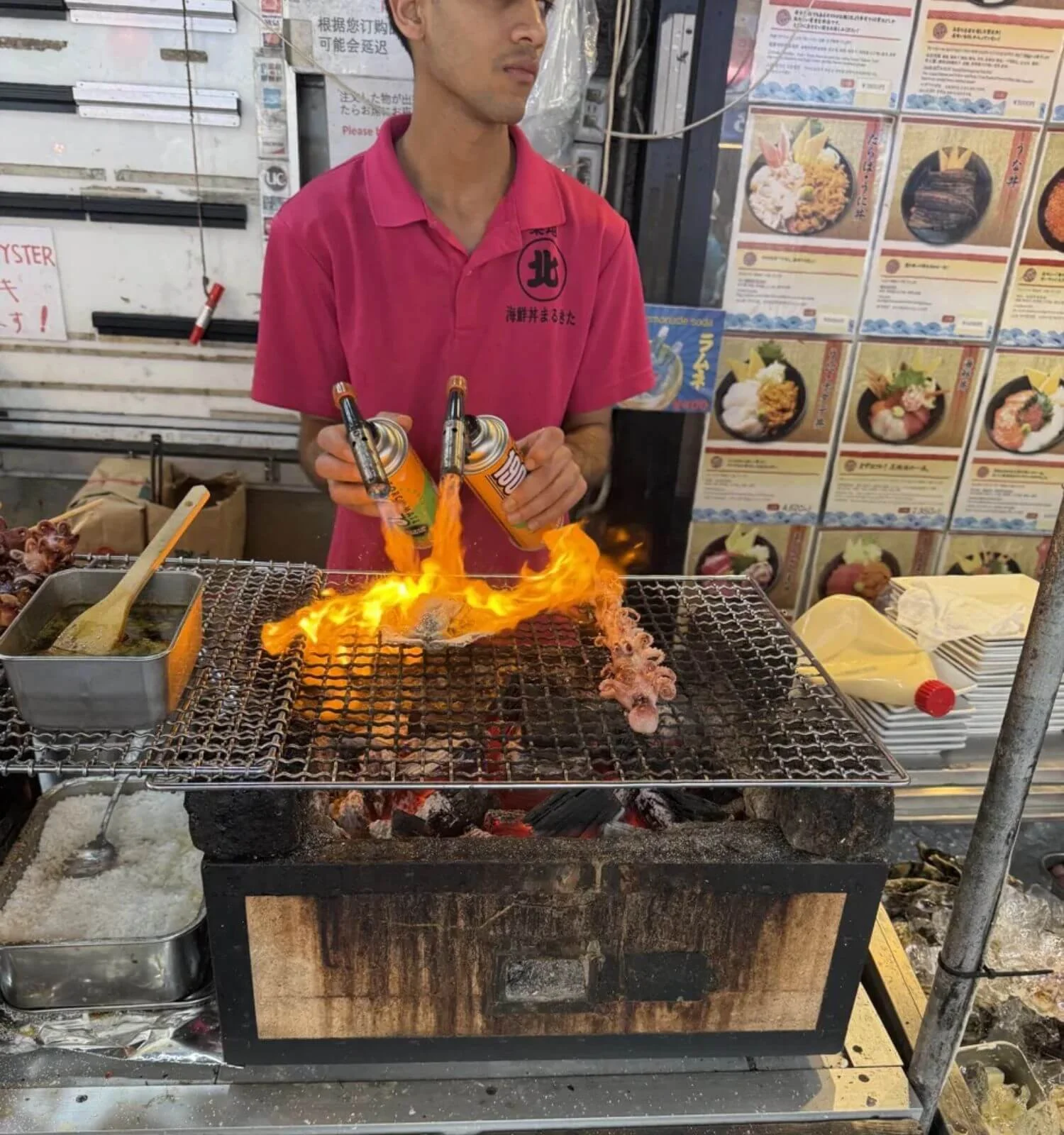 Market stall worker flame-searing scallop and octopus at a seafood stand in Japan