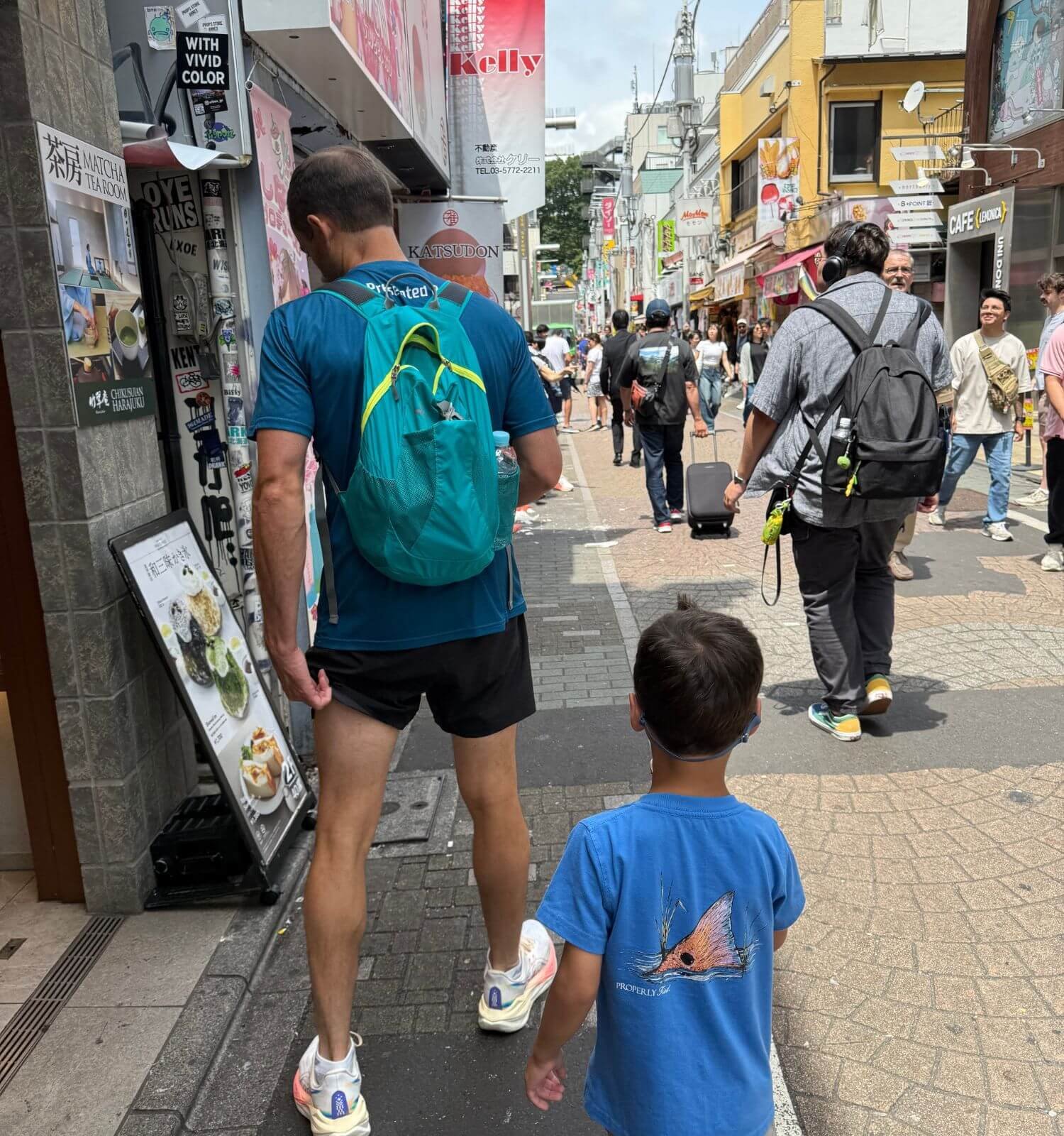 Father and son walking down a busy shopping street in Harajuku, Tokyo, wearing a daypack