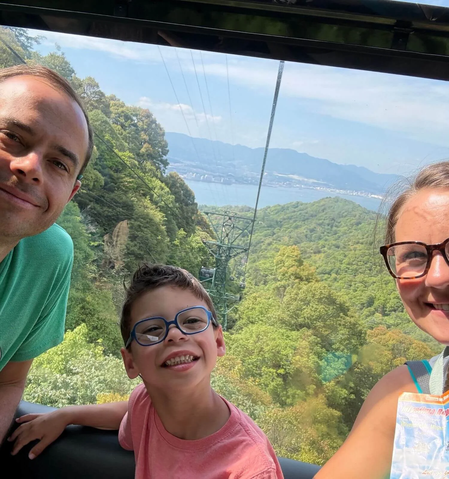 Family selfie while in gondola of the Miyajima ropeway with Hiroshima skyline in the background.