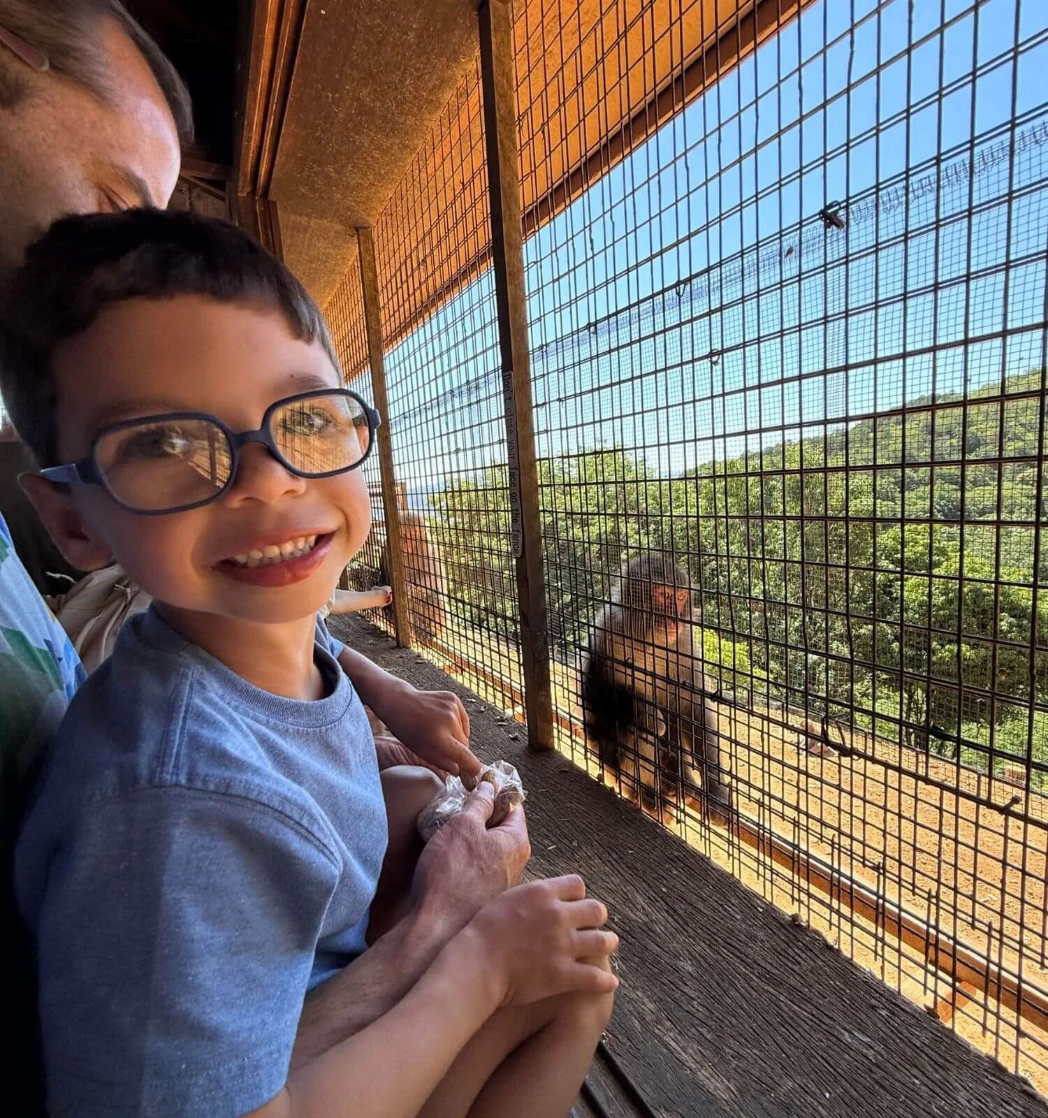 A young boy smiling inside the feeding shelter at Arashiyama Monkey Park in Kyoto, Japan, with a monkey visible in the background.