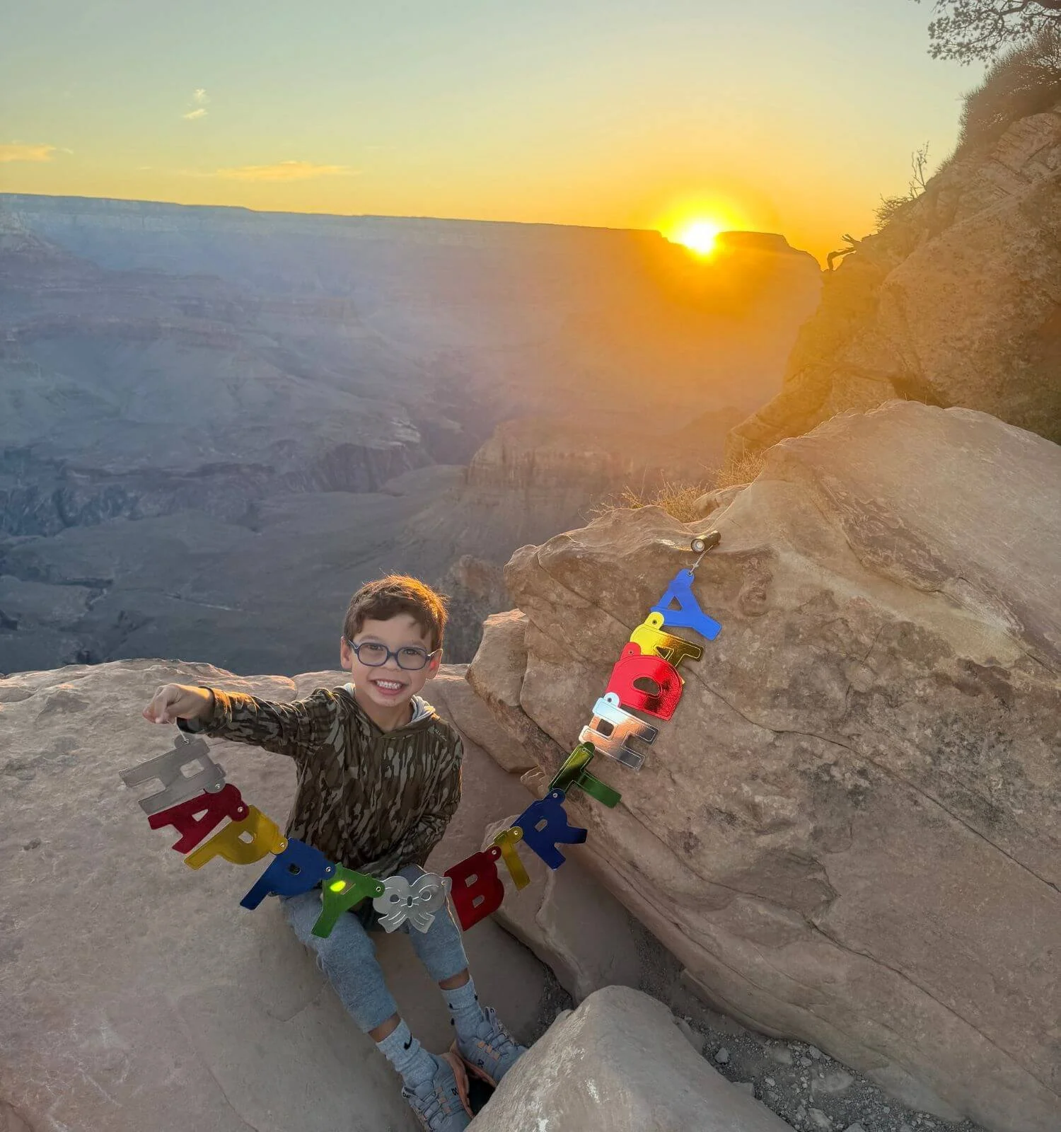 Boy holding a birthday banner at sunrise at ooh aah point on the South Kaibab trail in the Grand Canyon National Park in Arizona, USA.
