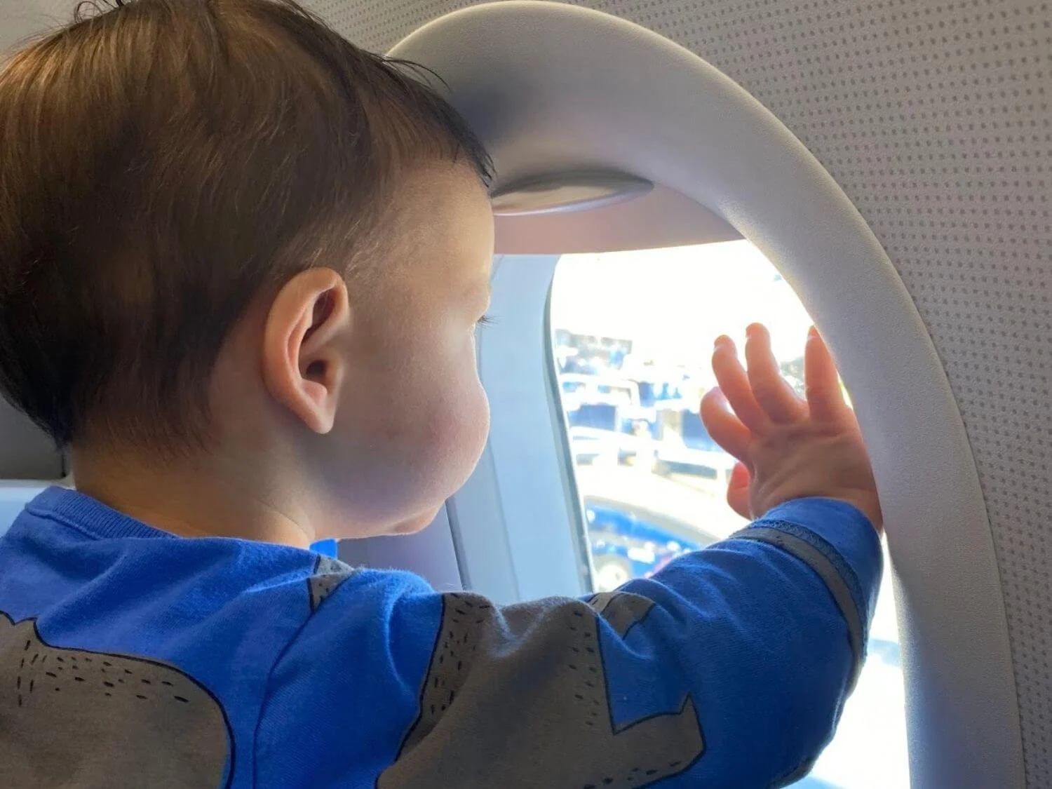 Young boy in a blue shirt looking out an airplane window before takeoff