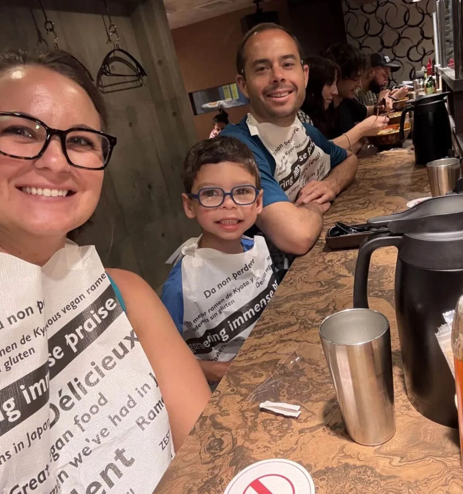 Family of three smiling together at a ramen restaurant counter in Kyoto, Japan