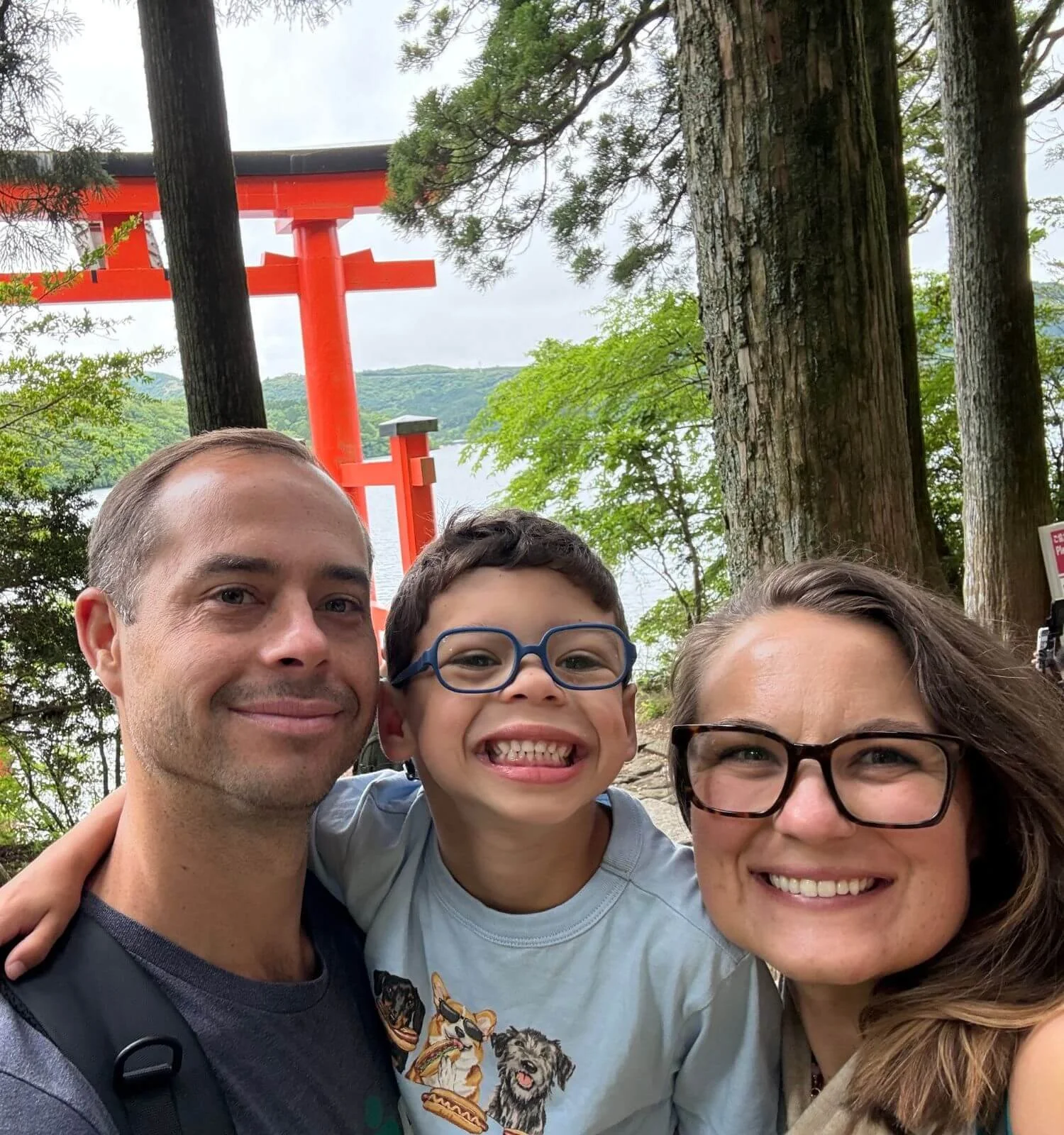 A family of three taking a selfie in front of the floating torii gate at Hakone Shrine, Japan.