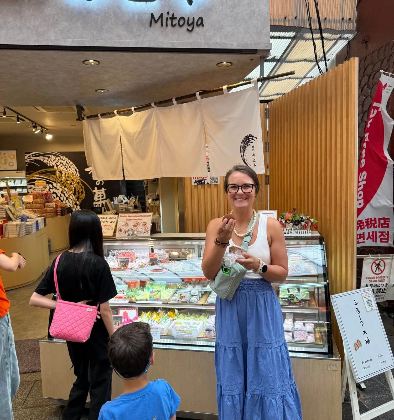 A woman smiling while holding gluten-free mochi at Kuromon Market in Osaka, Japan.