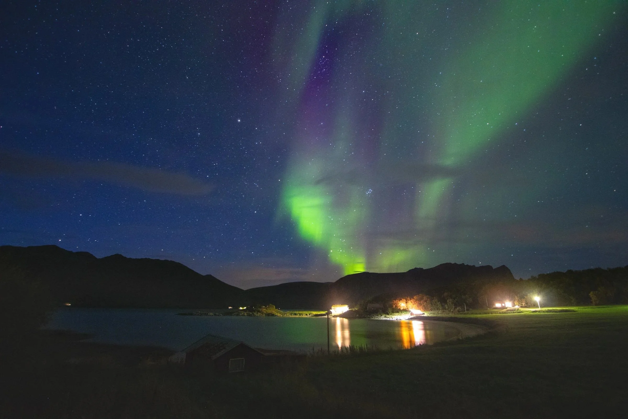 Nordlys over fjell og vann om natten, med stjerner på himmelen.