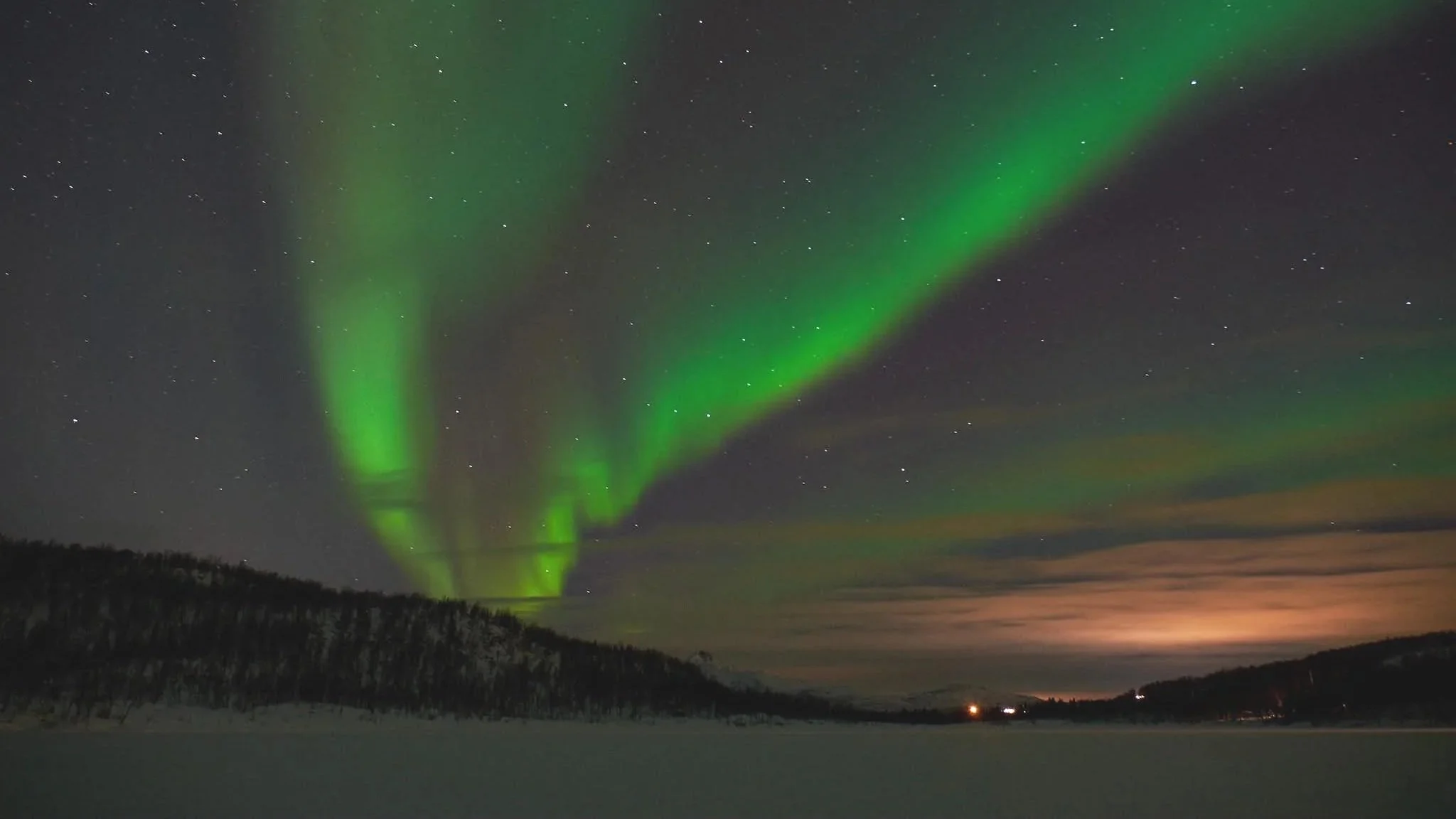 Nordlys over en fjell- og sjølandskap om natten med stjerner på himmelen.