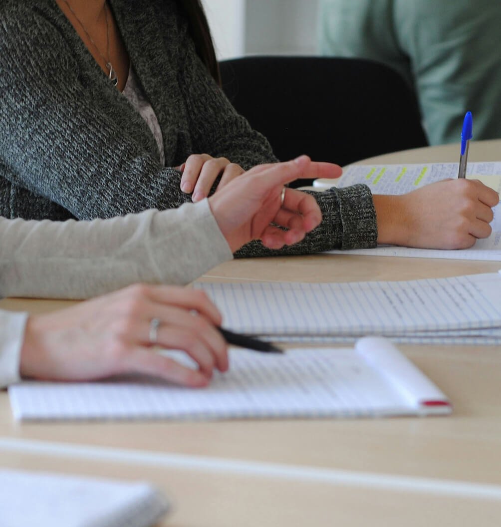 Students sitting at a table writing in notebooks during a class or training session.