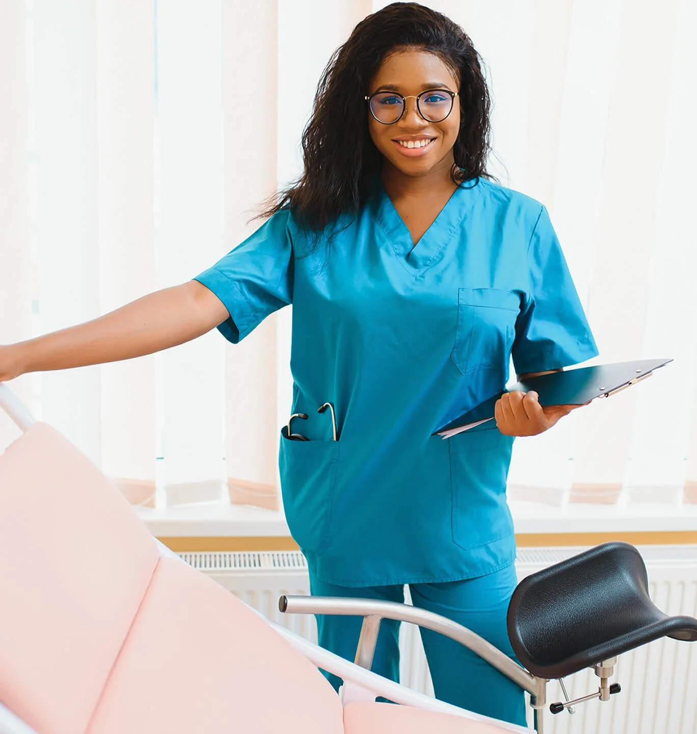 Healthcare professional in scrubs holding a clipboard and smiling in a clinical environment.