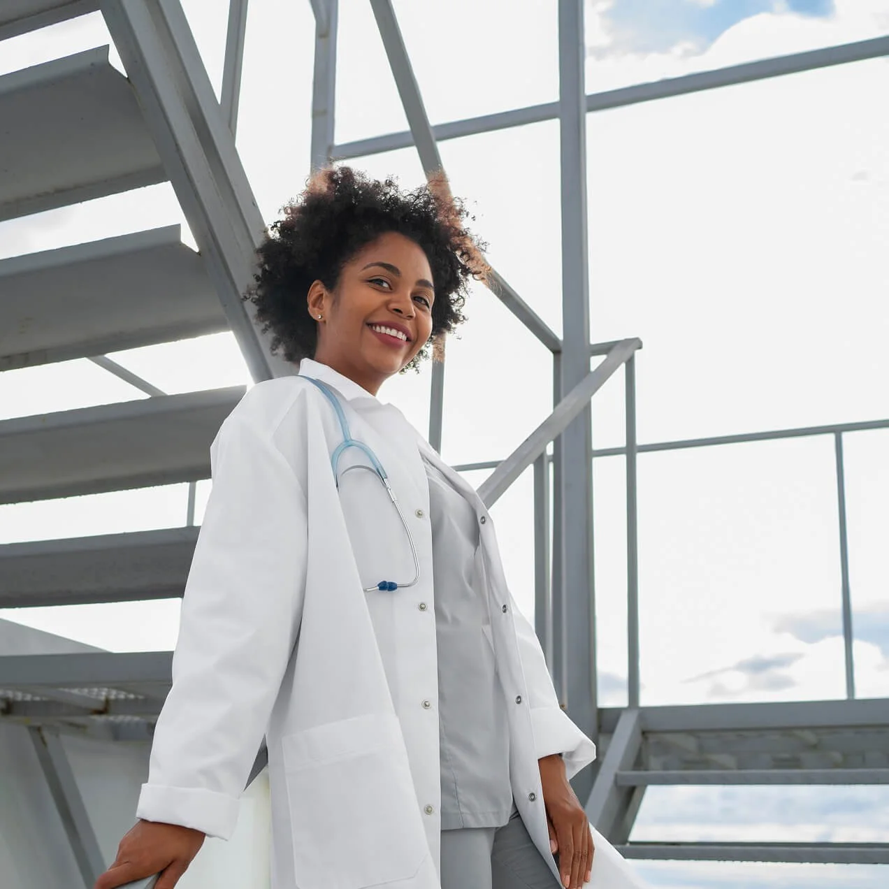 Healthcare professional wearing a lab coat standing near a hospital building.