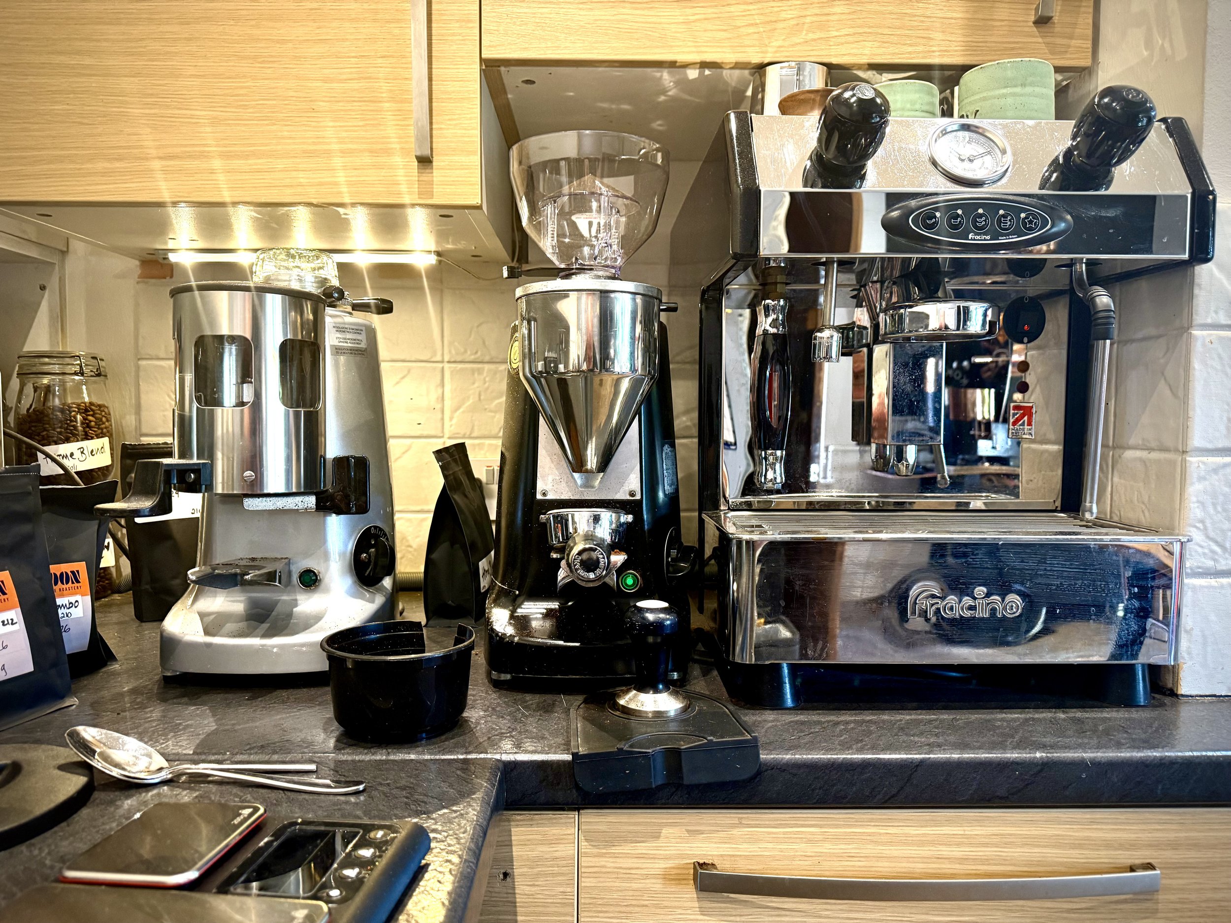 Coffee brewing station with an espresso machine, coffee grinder, and a coffee roaster on a black countertop.