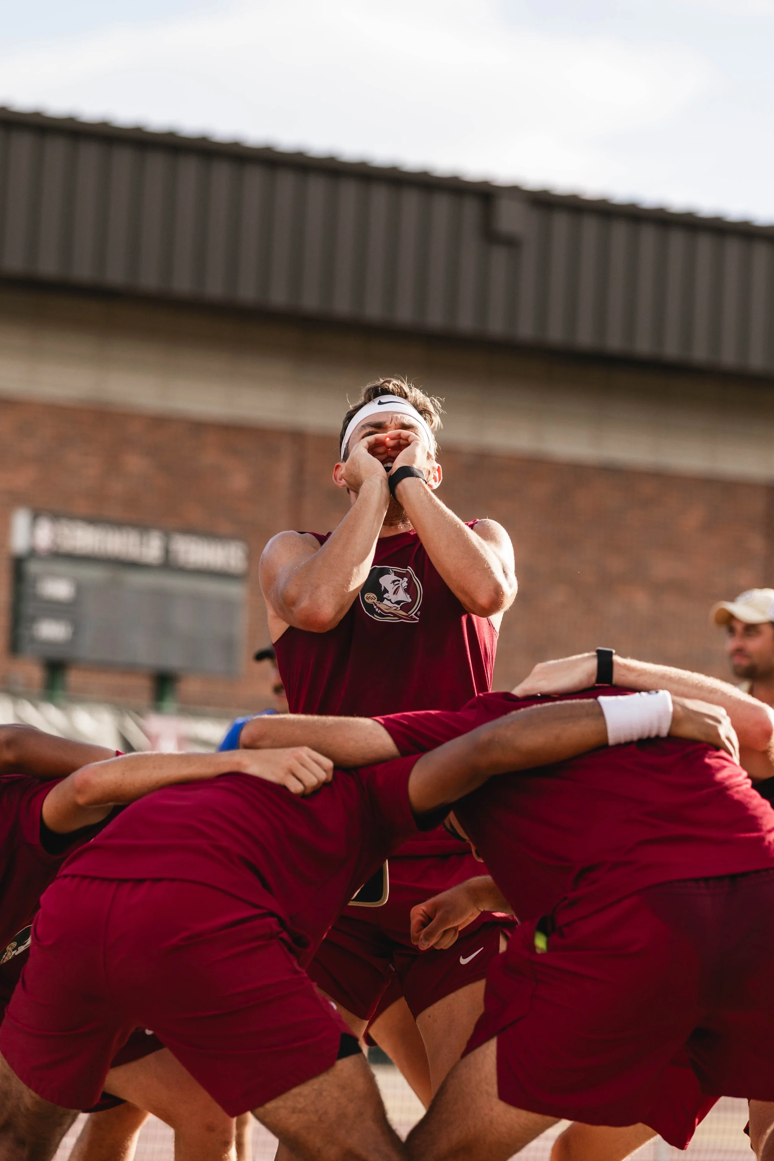 A group of male athletes in maroon uniforms participating in a rugby scrum during a game.