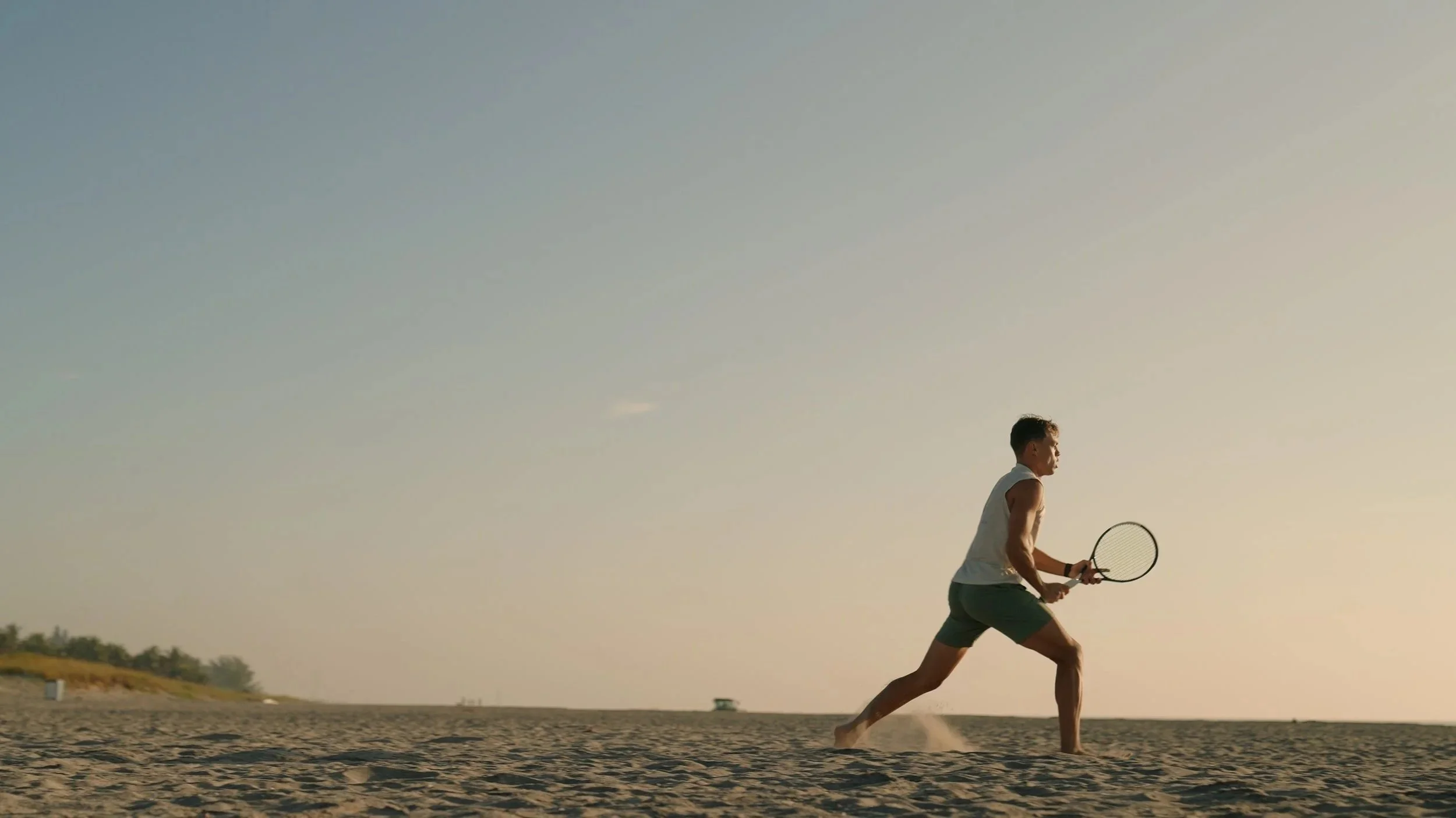 A man playing tennis on a sandy beach during sunset or sunrise.