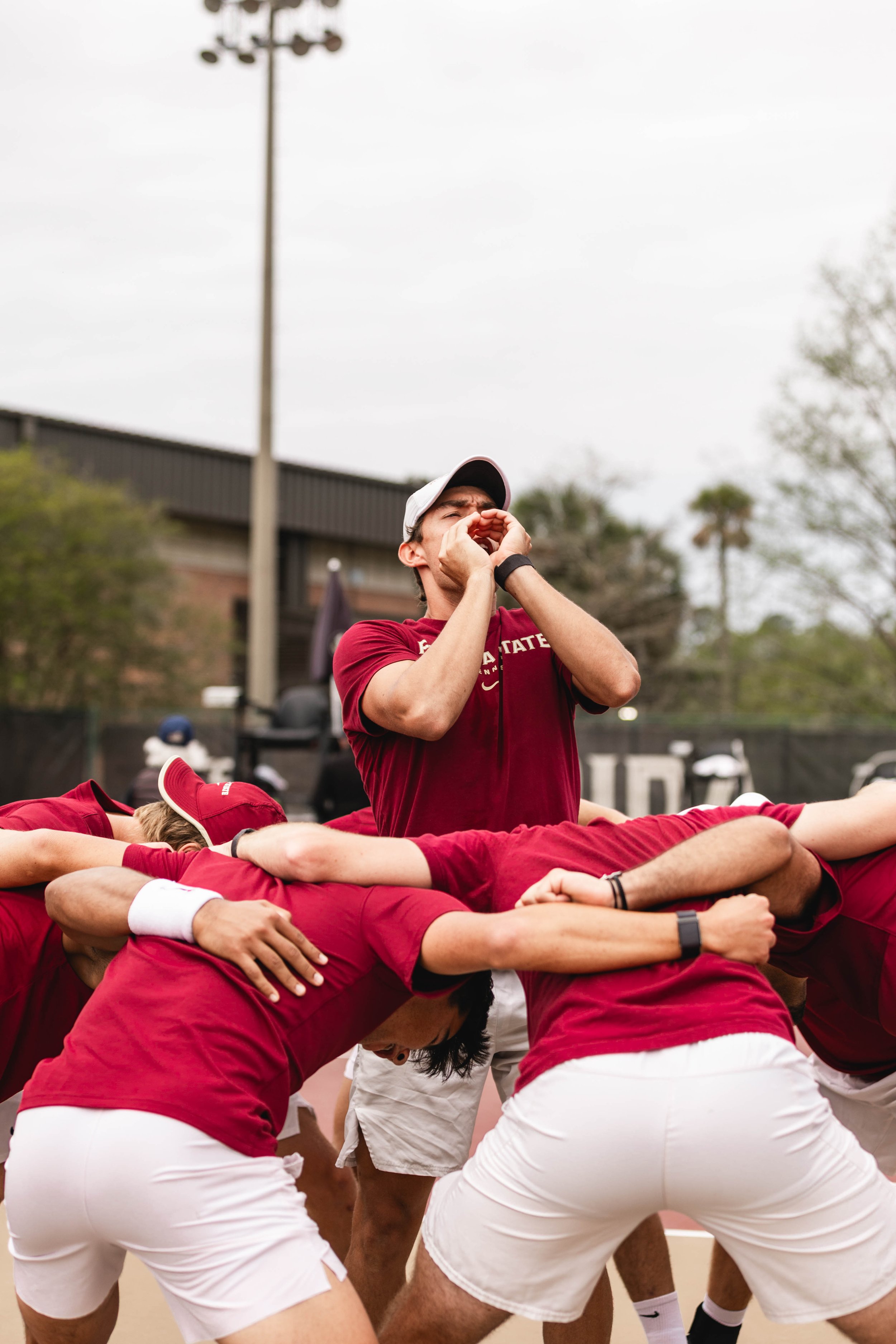A group of people dressed in red and white sportswear forming a human pyramid on a court, with one person in the middle shouting into a megaphone.