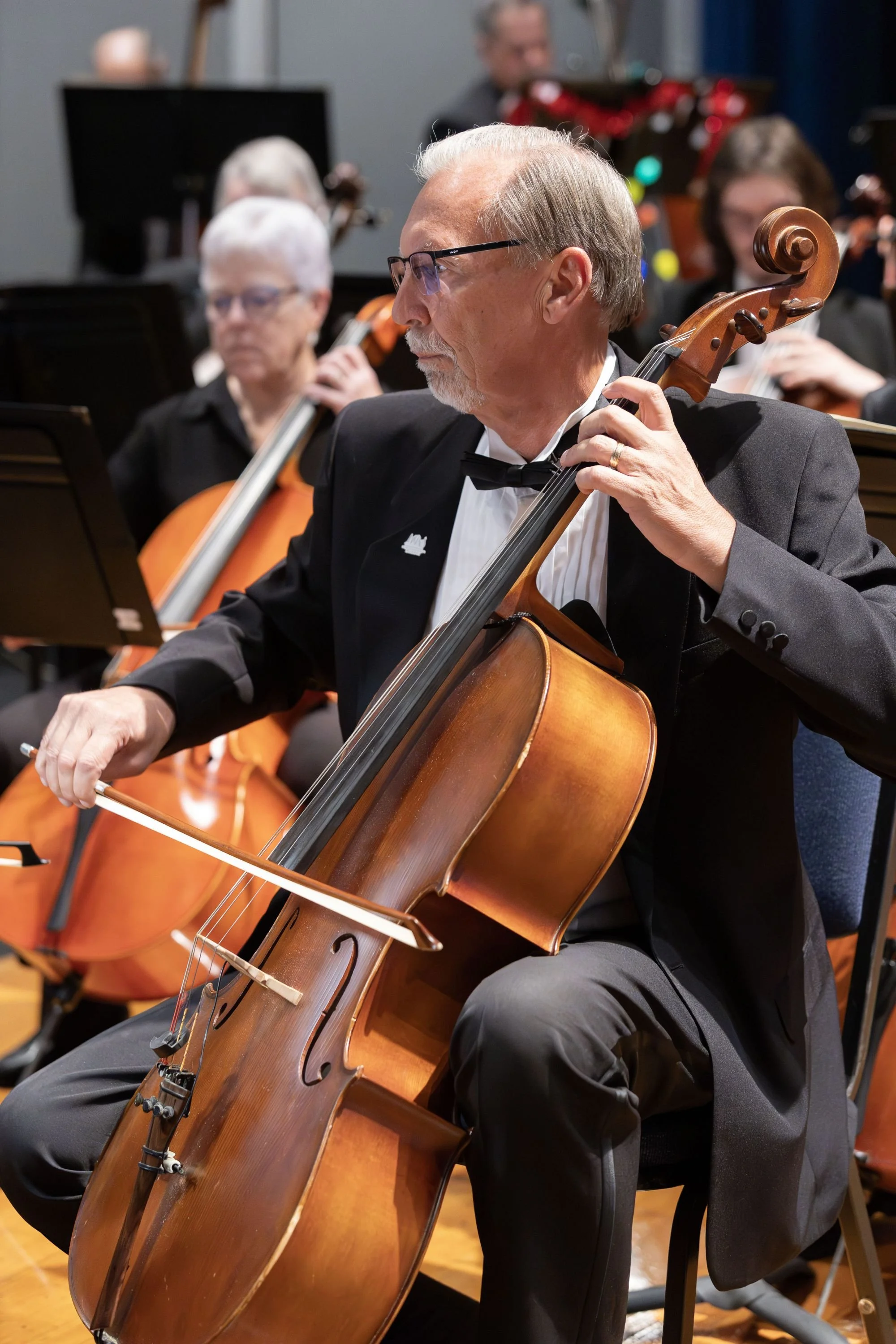 An elderly man in a tuxedo playing a cello during a symphony performance.