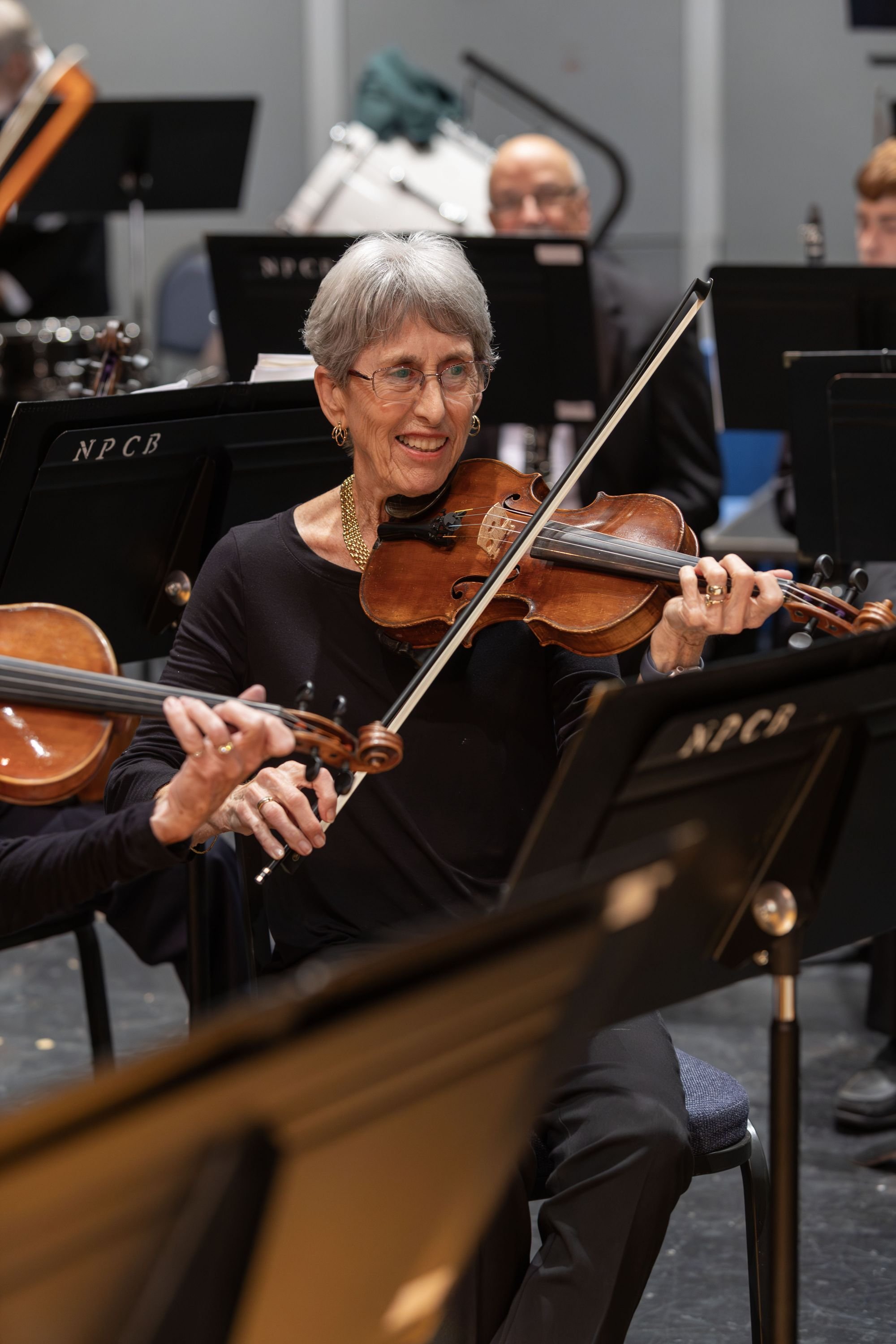 An elderly woman playing the violin during an orchestra performance.