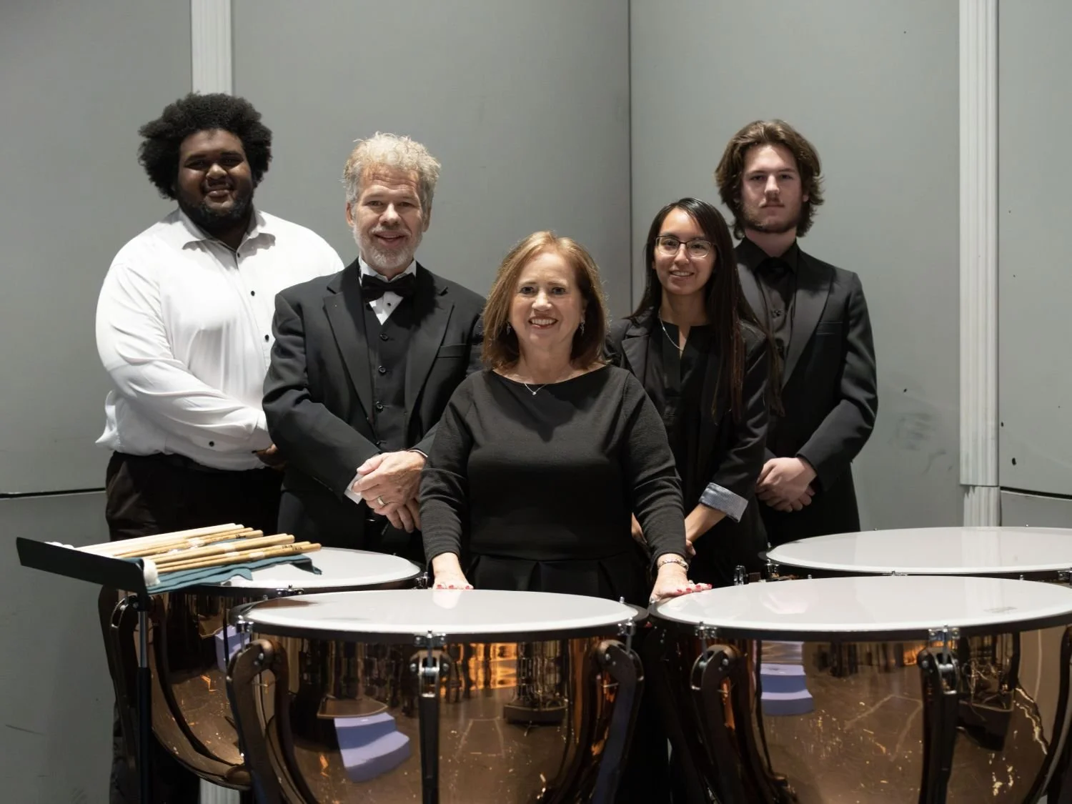 A group of five musicians in formal attire posing indoors, with percussion instruments in front.
