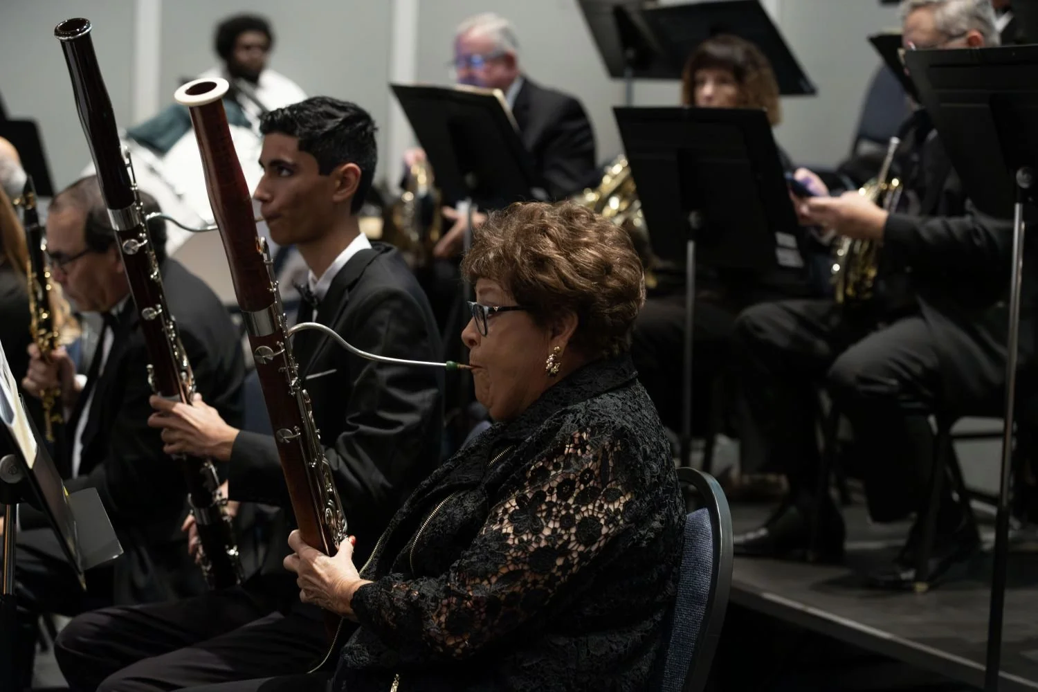 Orchestra members performing, including a woman playing the bassoon in the foreground, with other musicians in the background.