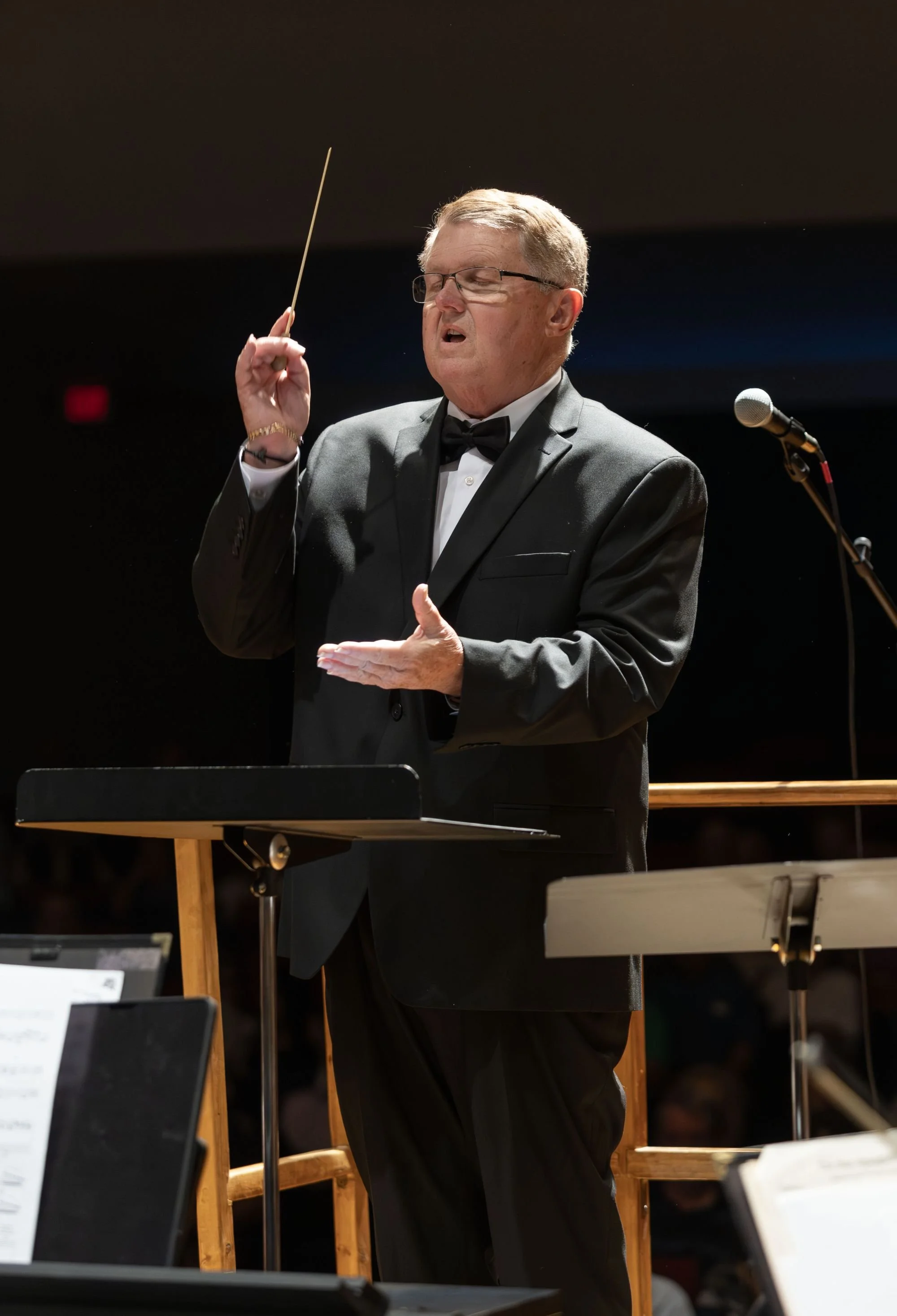 A man in a tuxedo conducting an orchestra.