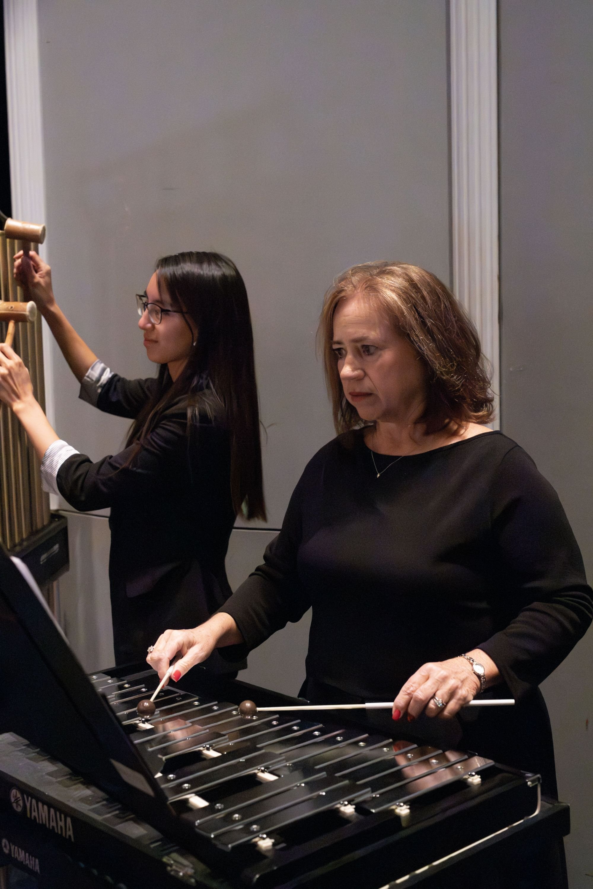 Two women, one playing a vibraphone and the other playing a xylophone, performing together in an indoor setting.