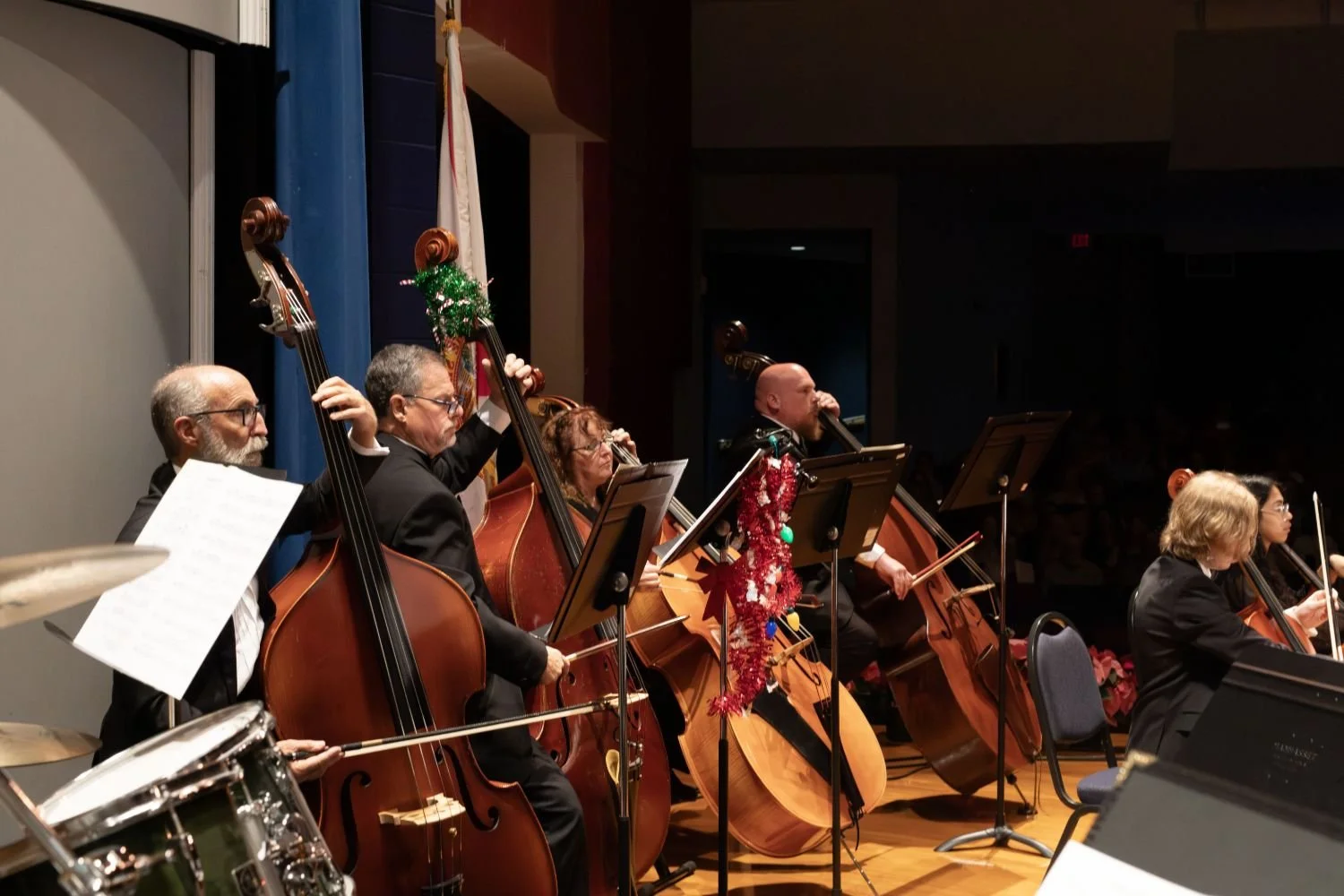 A group of musicians playing string instruments on stage during a Christmas concert, with holiday decorations on their instruments.