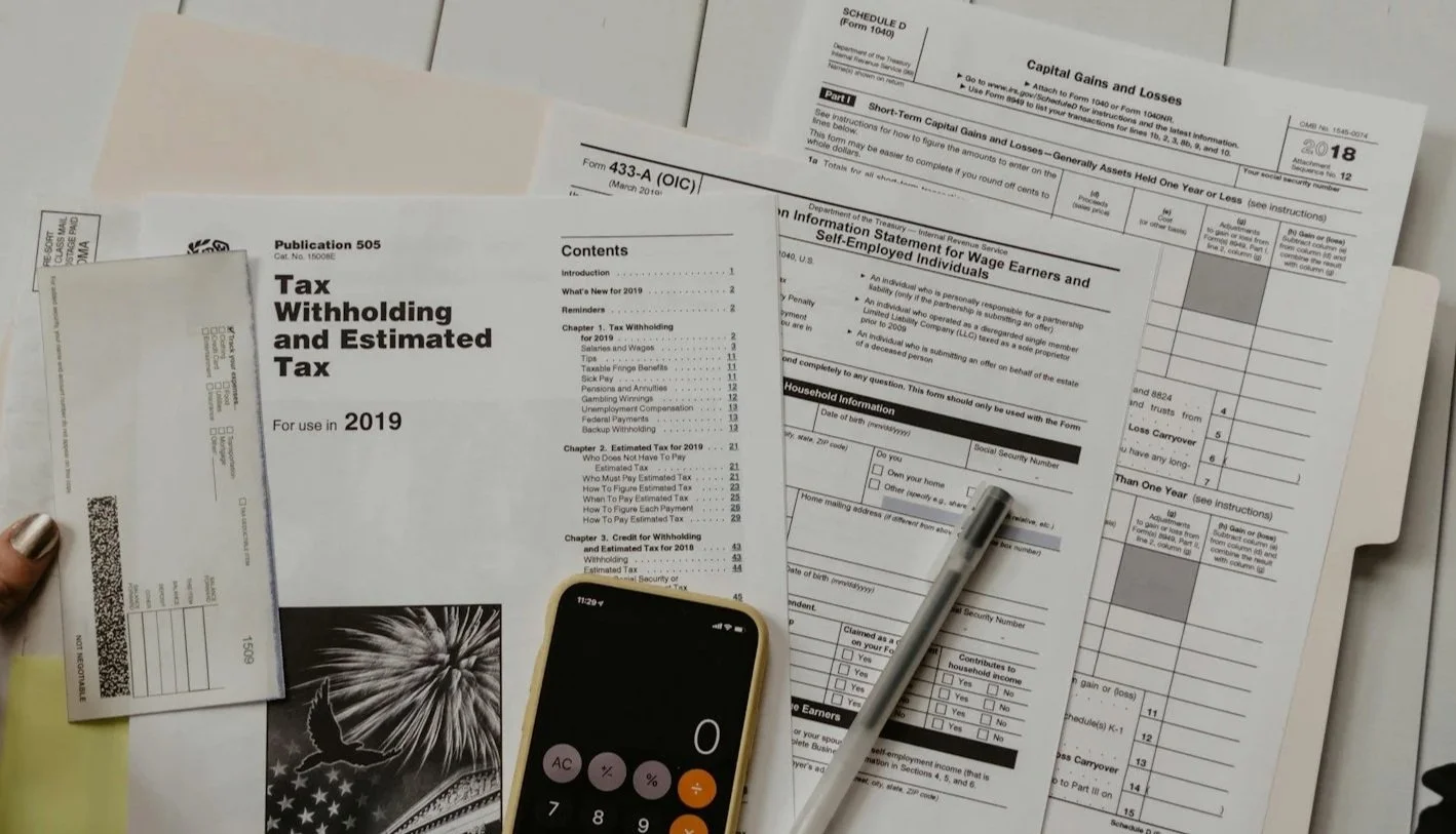 Collection of tax documents, including Tax Withholding and Estimated Tax for 2019, an information form for wage earners, a calculator, a pen, and a smartphone with a calculator app, all laid out on a flat surface.