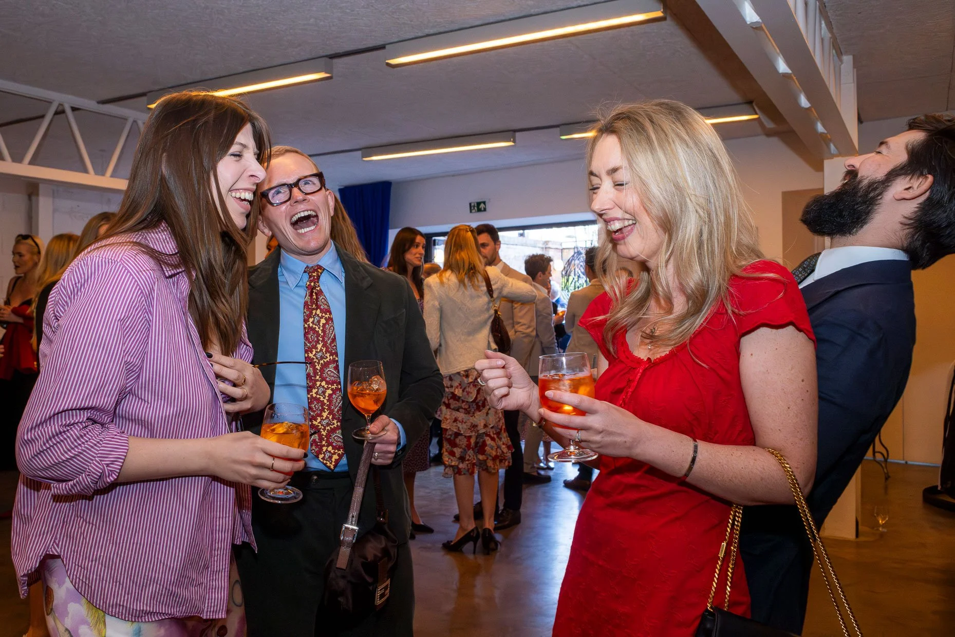 People enjoying a social gathering, laughing and talking while holding drinks.