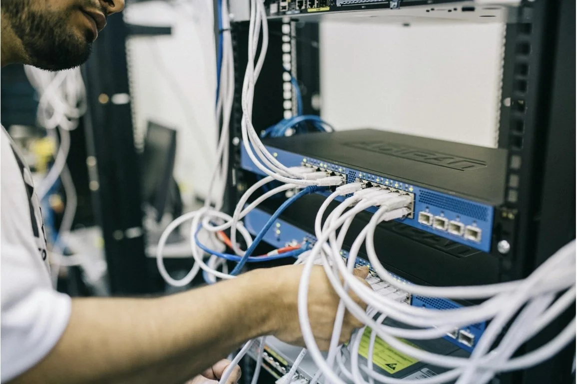 Technician working on network cables connected to a blue network switch or router in a server rack.