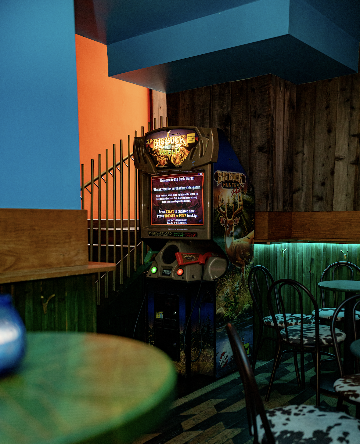 An arcade game machine titled "Big Buck World" in a dimly lit room with colorful walls and chairs nearby.