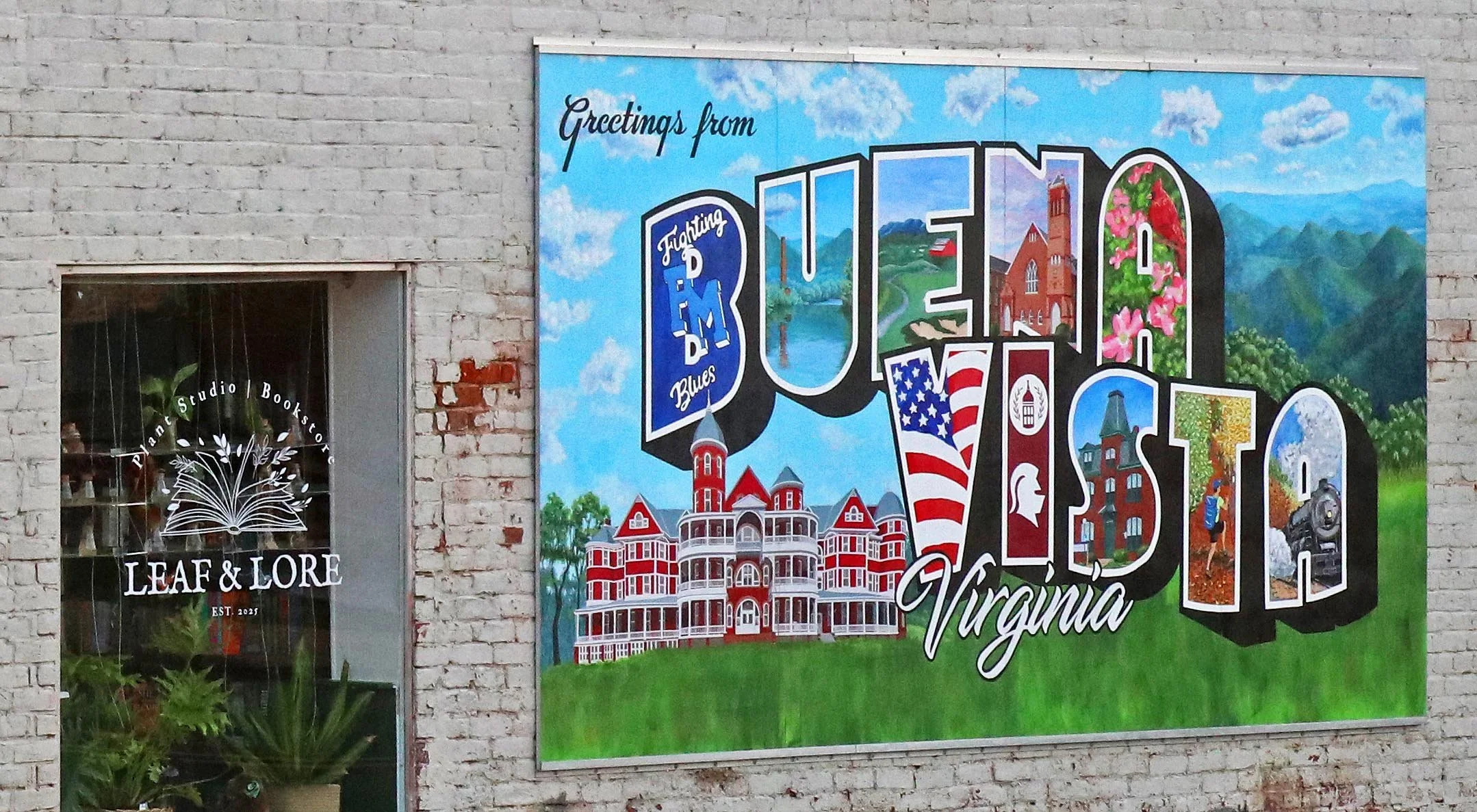 Large colorful sign on white building that says "Greetings from Buena Vista, Virginia" on left window with plants in from Leaf & Lore Plant Studio & Bookstore